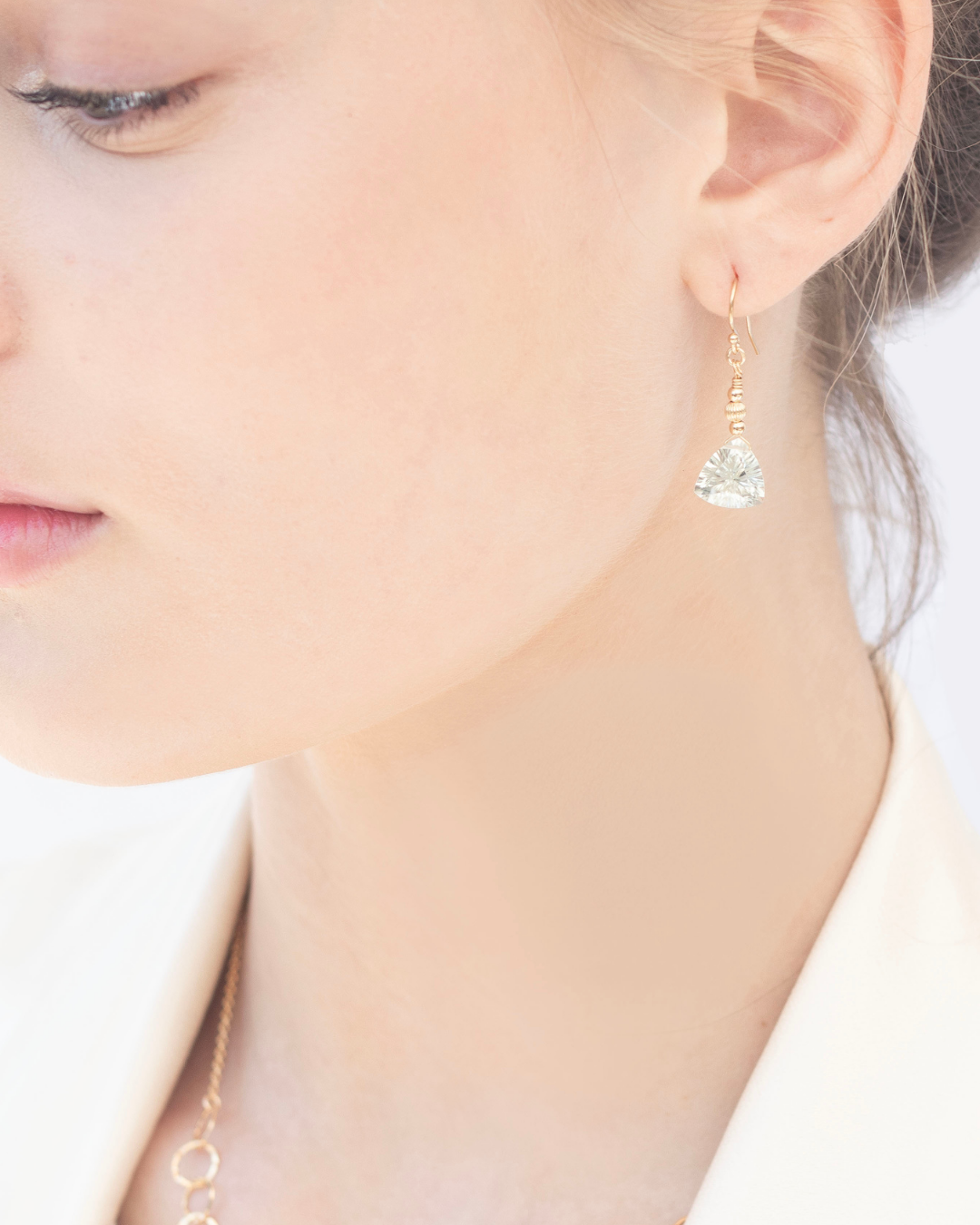 Close-up of a person wearing gold earrings with green amethyst faceted gemstone.