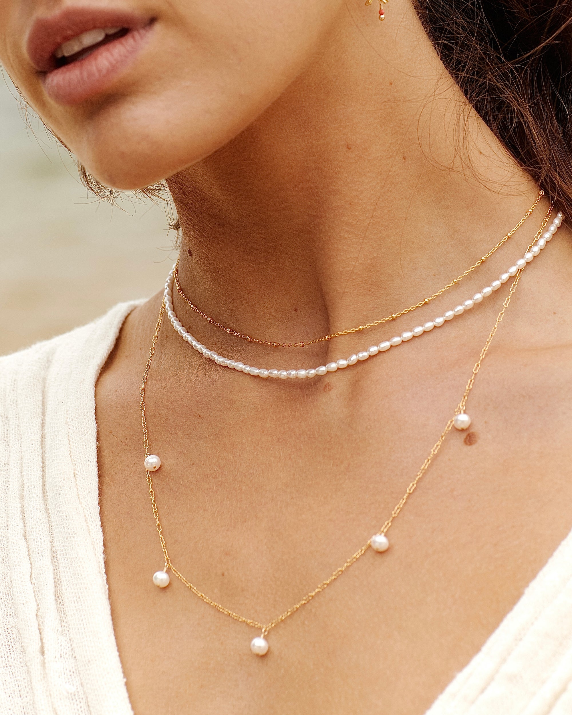 Close-up of a person wearing a delicate gold choker necklace layered with two pearl necklaces with a blurred background