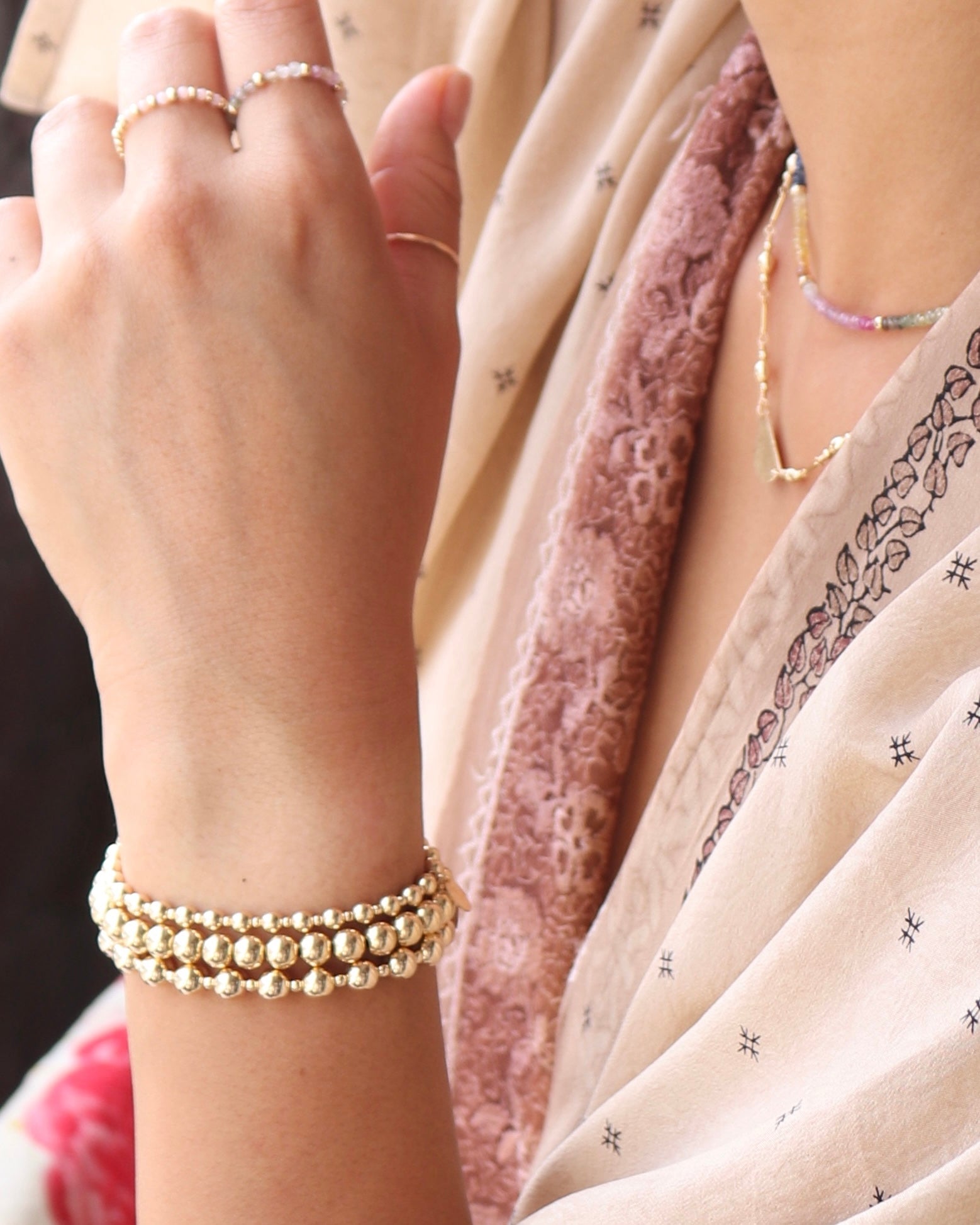 Close-up of a woman wearing gold bracelets. rings and necklaces with a blurred background