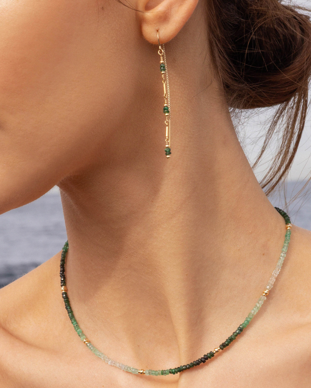 Close-up of a person wearing green emerald beaded earrings and necklace with blurred background