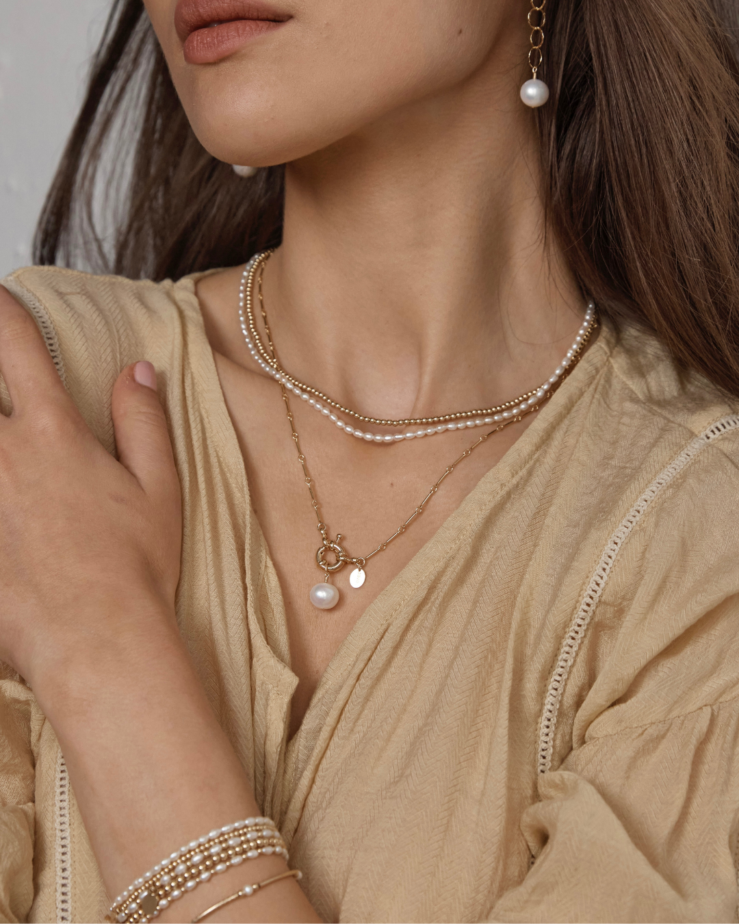 Close-up of a woman wearing pearl and gold jewellery including a pearl pendant necklace.