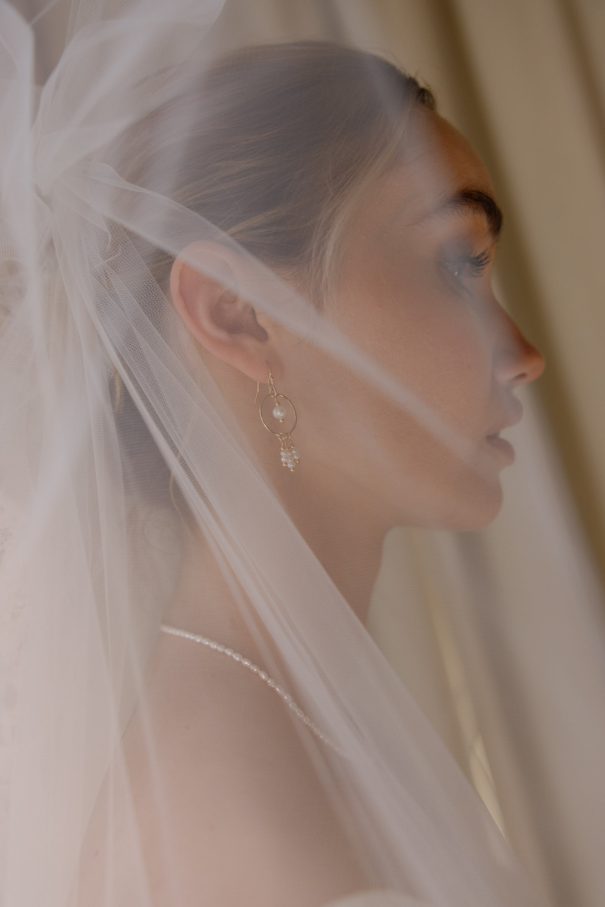 Woman wearing a veil with a soft focus background and pearl and gold jewellery.