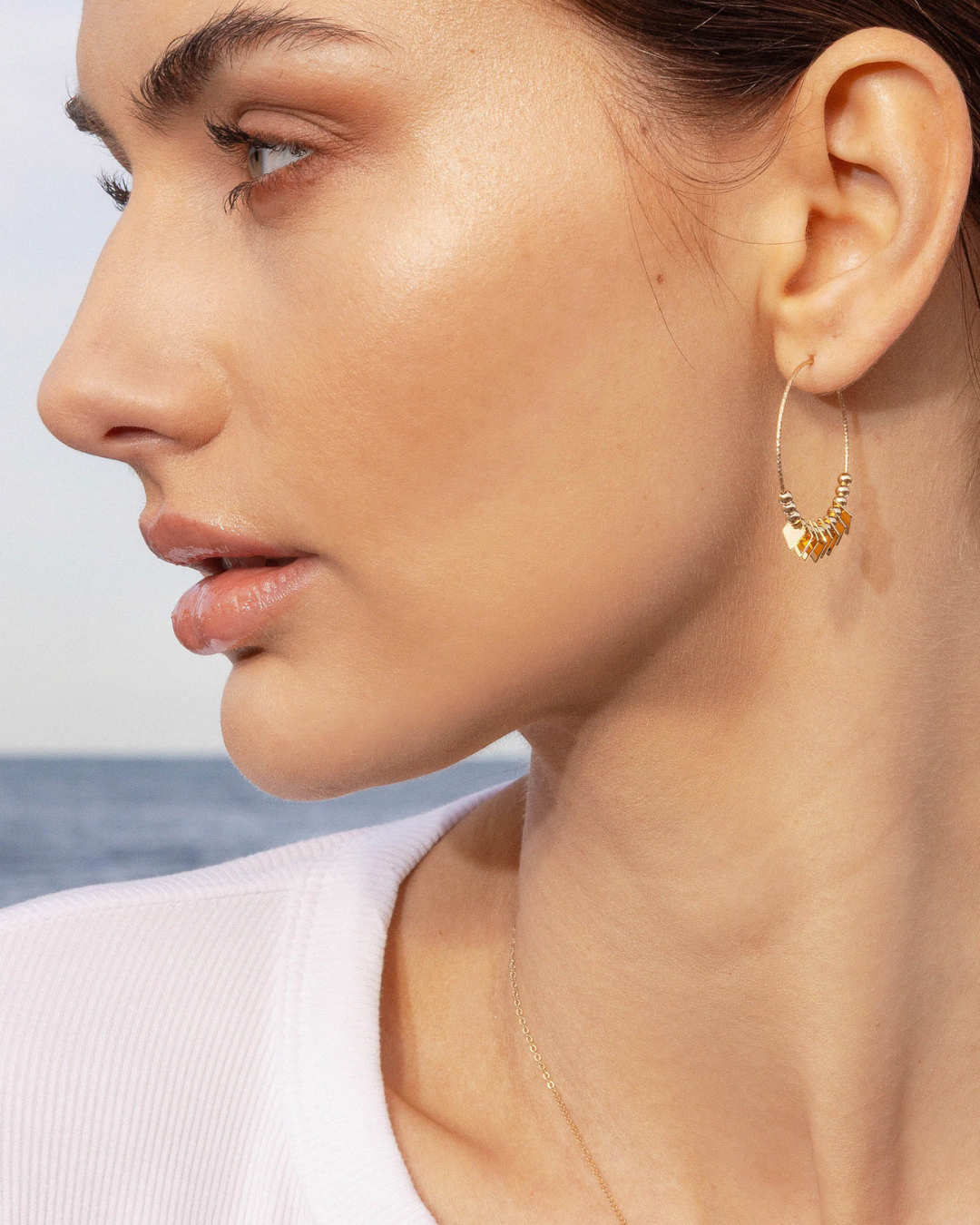 Close-up of a woman wearing gold hoop earrings with a blurred background