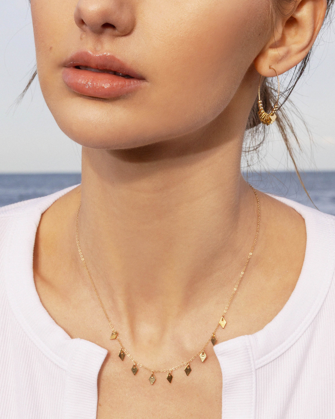 Close-up of a person wearing a gold hoop earring and a delicate gold necklace with a blurred background