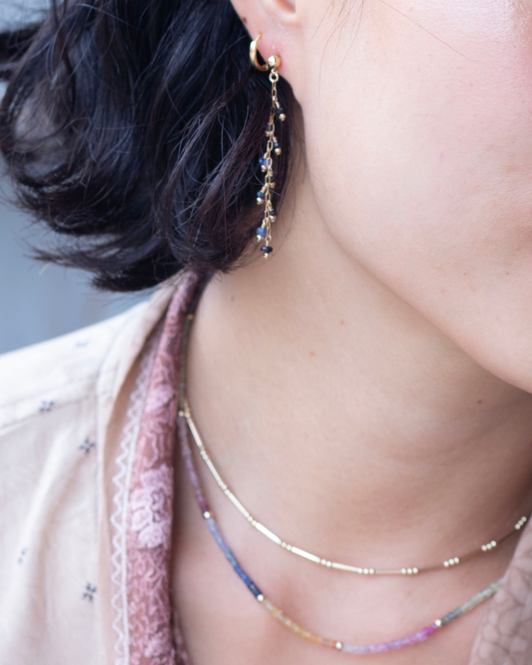 Close-up of a person wearing layered necklaces and an earring with a blurred background