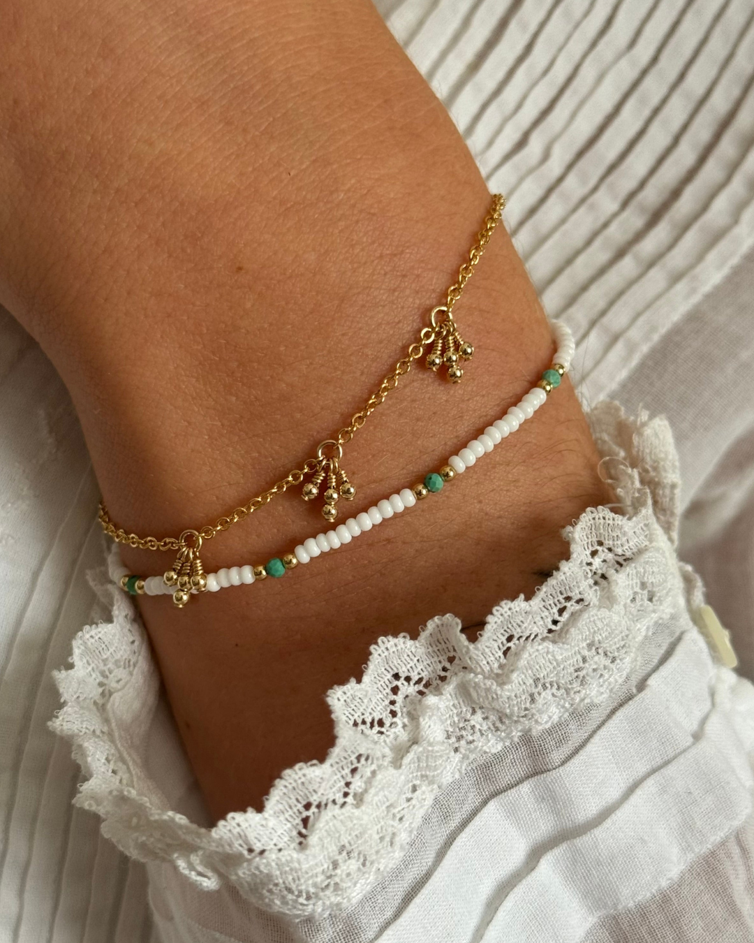 Bracelets with turquoise beads on a person's wrist against a white lace garment.