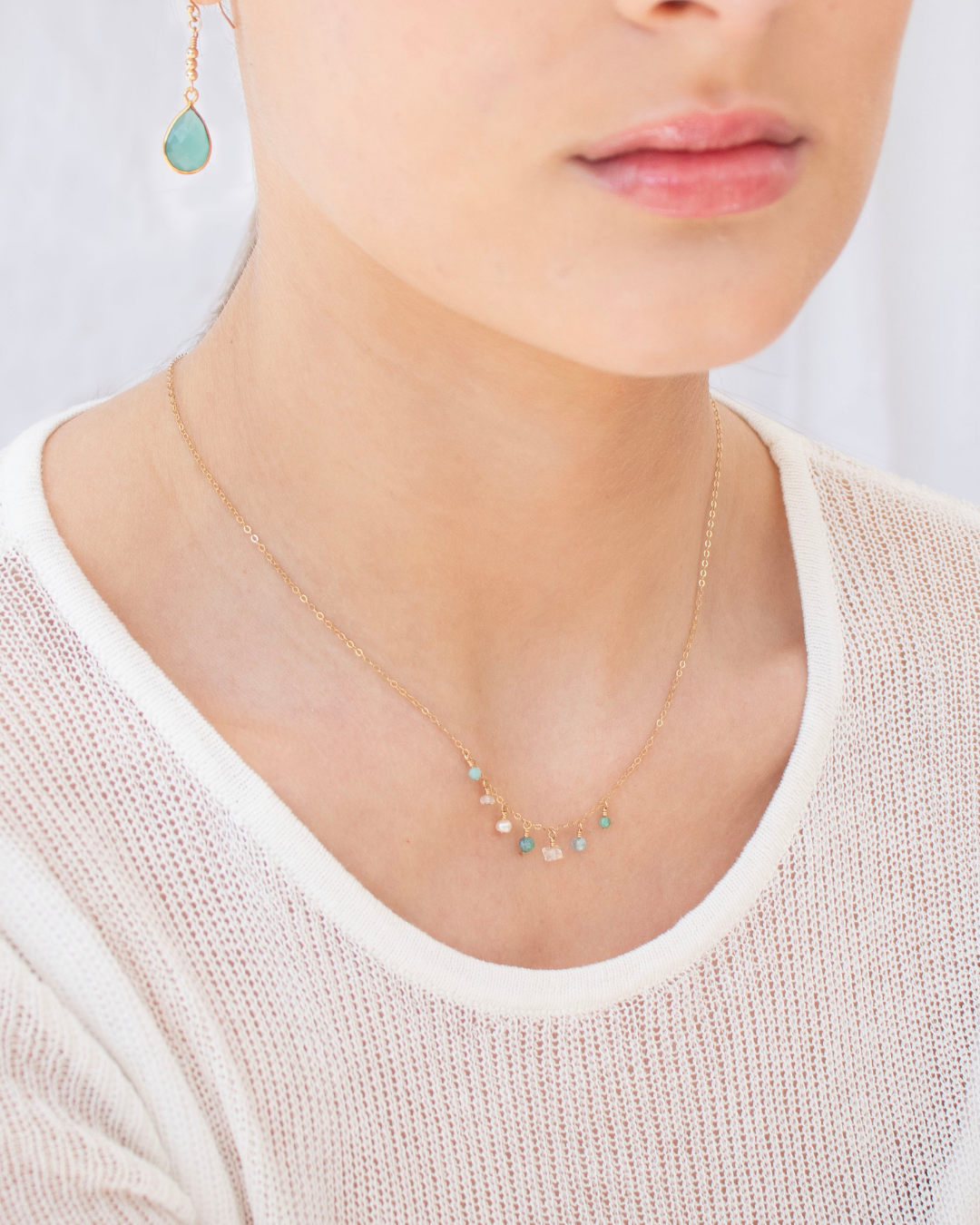 Necklace with small gemstones worn by a woman with a pair of chalcedony earrings against a neutral background