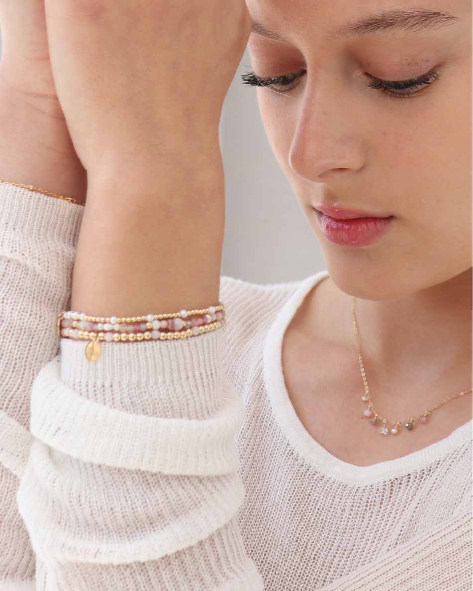 Close-up of a person wearing multiple bracelets and a necklace on a neutral background