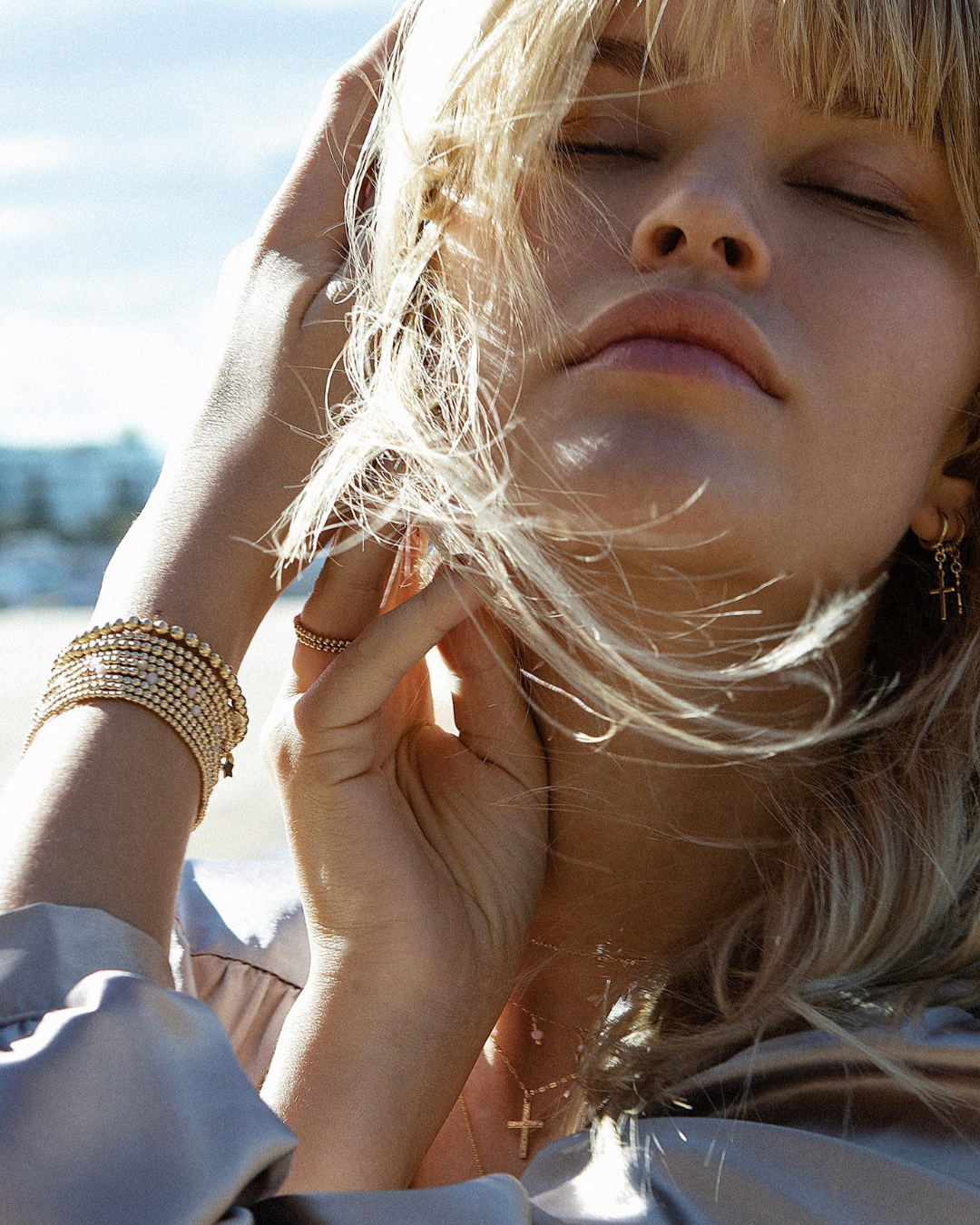 Woman with blonde hair and gold jewelry against a blurred natural background
