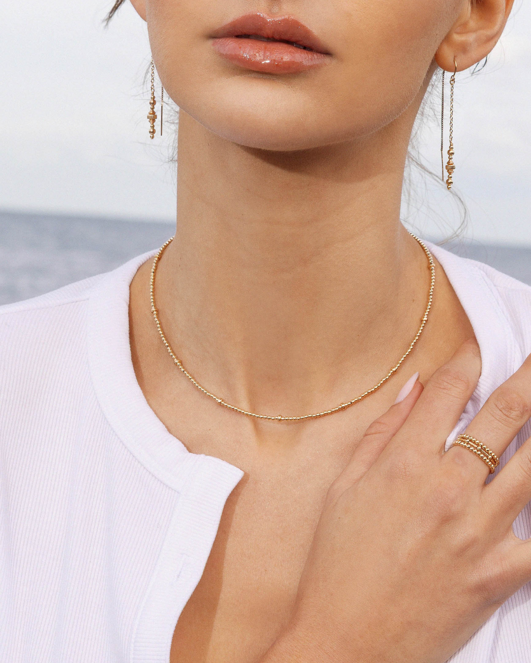 Close-up of a person wearing a gold necklace and earrings with a blurred background