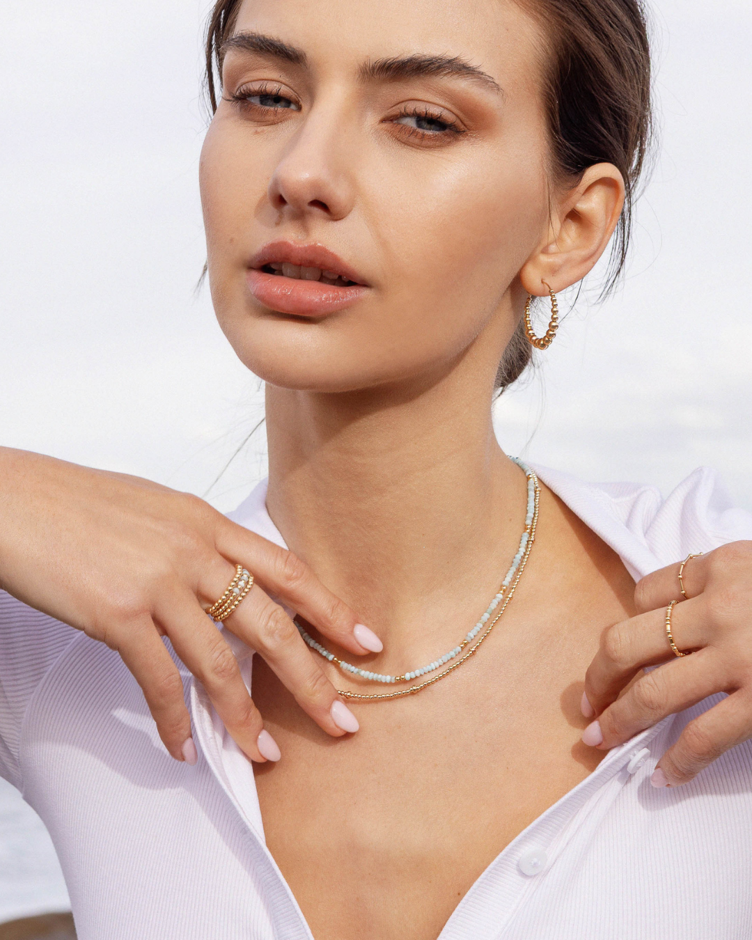 Woman wearing a gold necklace and hoop earrings with a white background