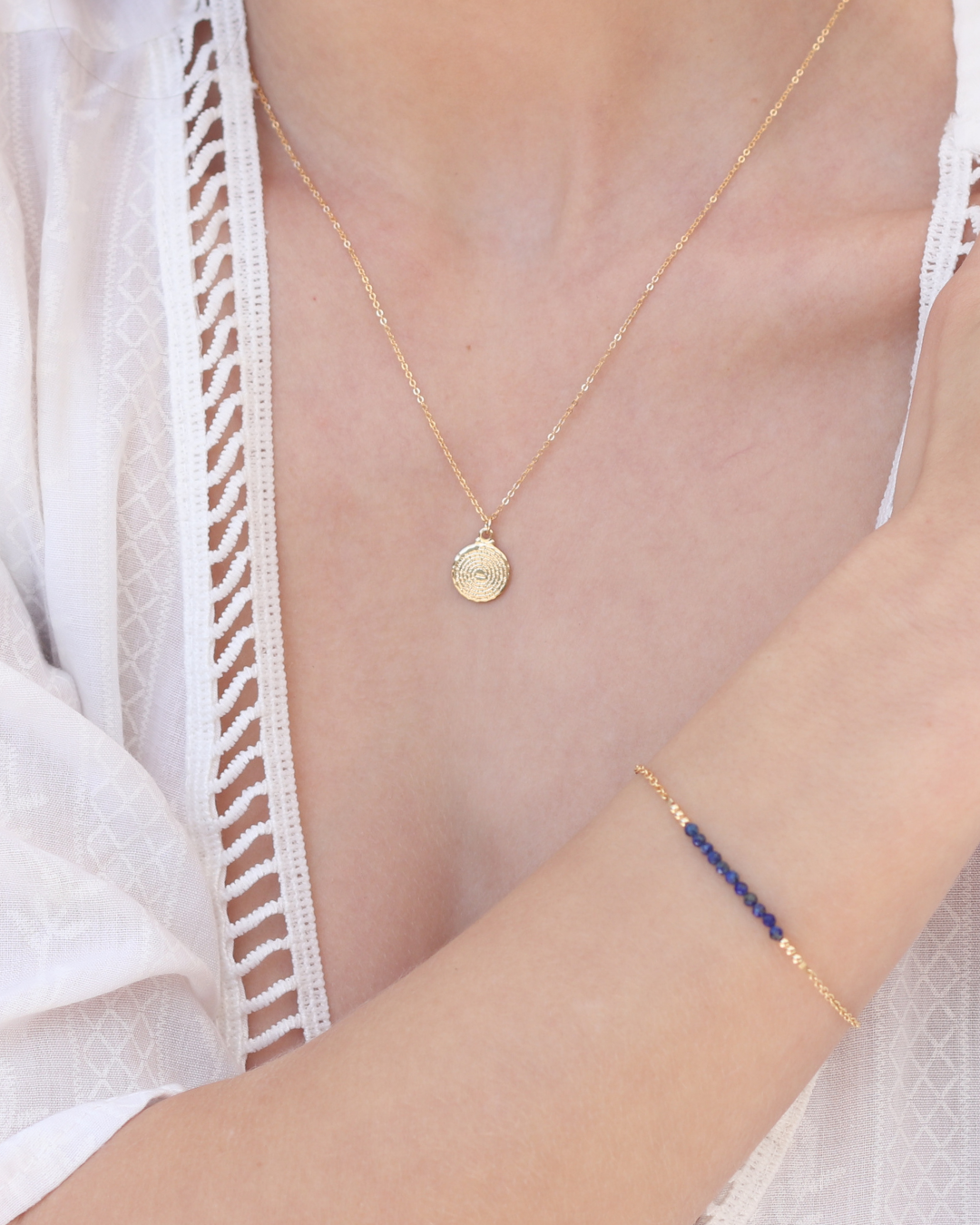 Gold necklace and bracelet on a person wearing a white lace top