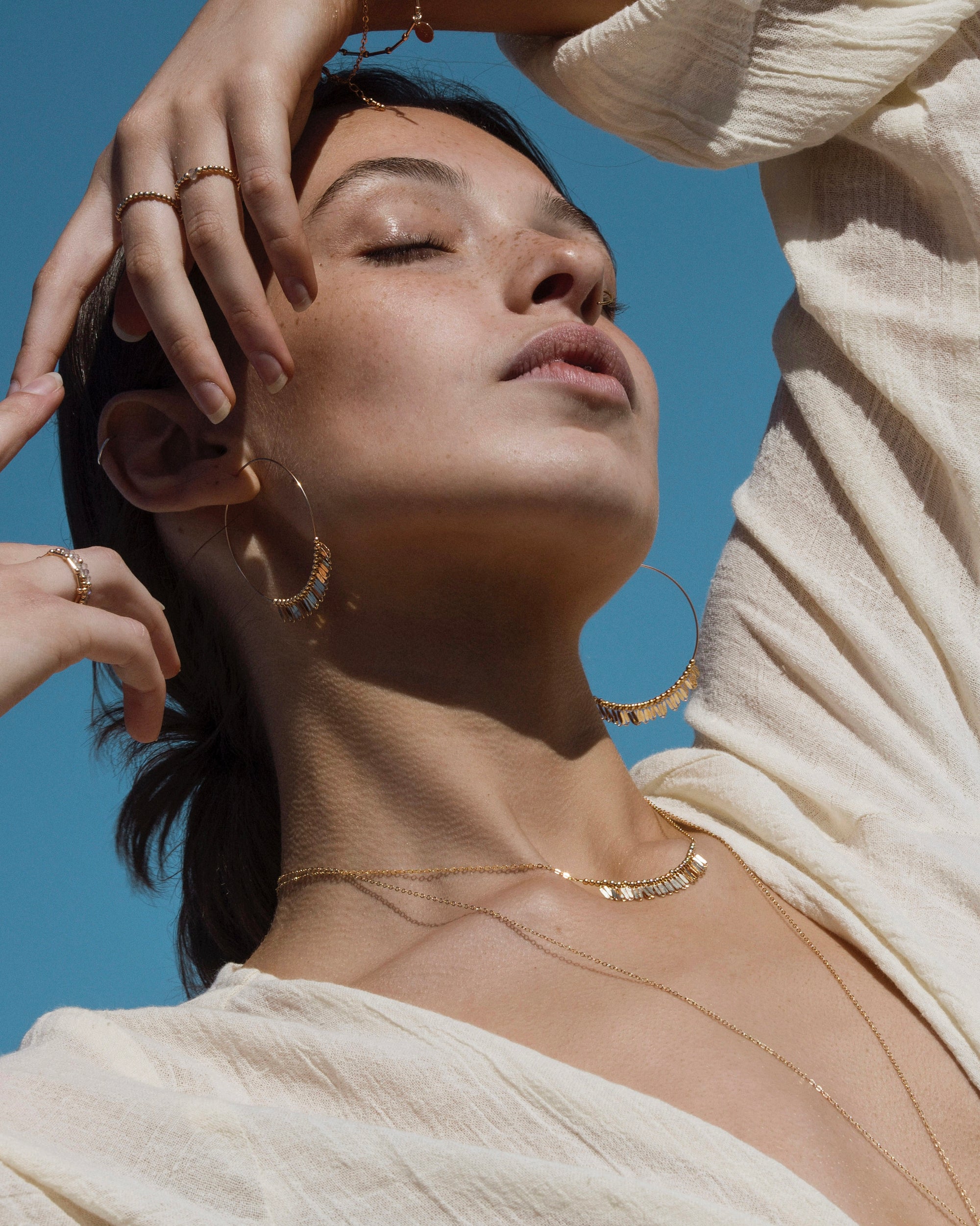 Woman wearing gold jewelry against a blue sky