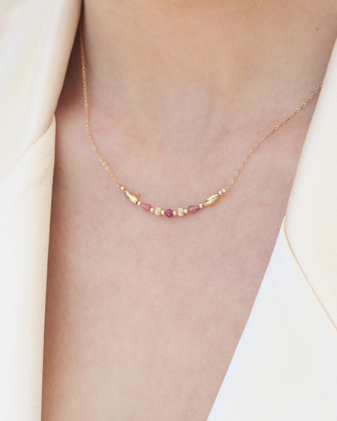 Close up of a woman's neck wearing a delicate gold necklace with pink tourmaline gemstones