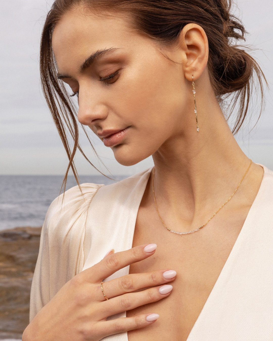 Woman wearing gold herkimer diamond jewellery with a blurred coastal background