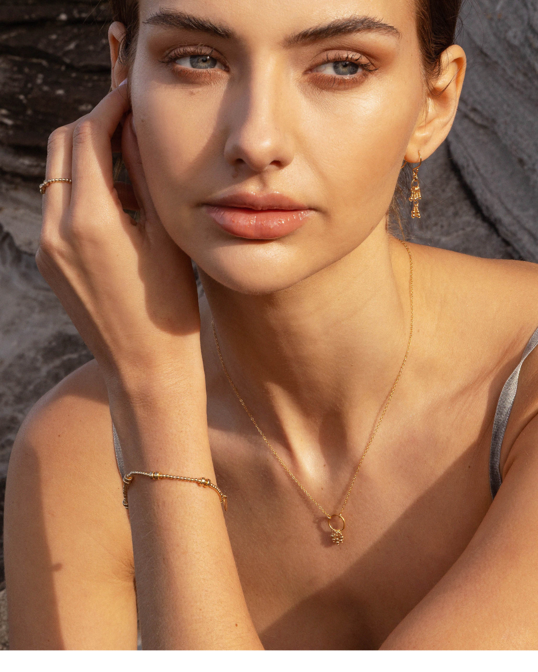 Close-up of a woman wearing a gold blue topaz necklace with gold earrings, bracelet, and ring against a natural background