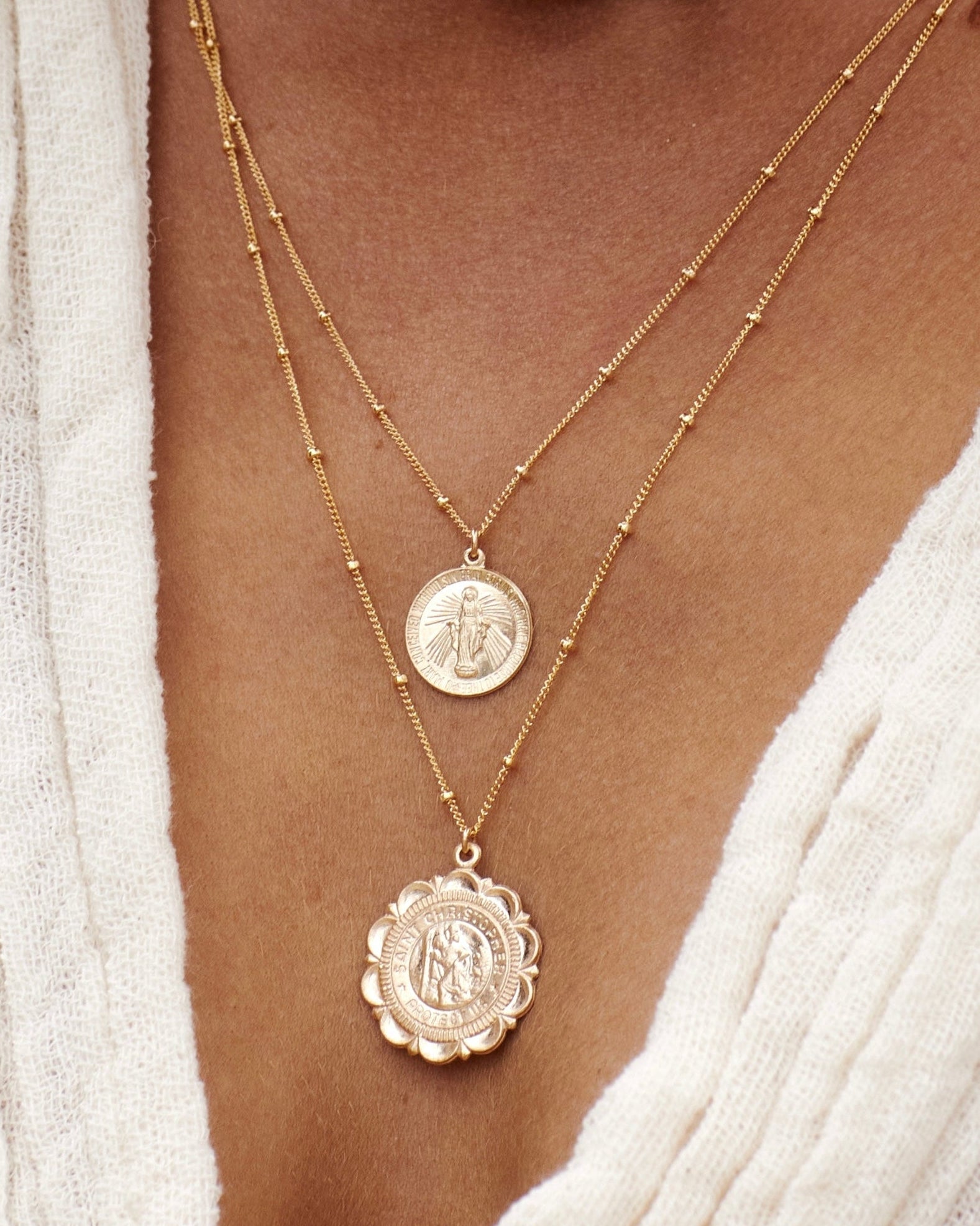 Close up of a woman wearing a white dress with gold necklaces with a Mary and Saint Christopher pendant