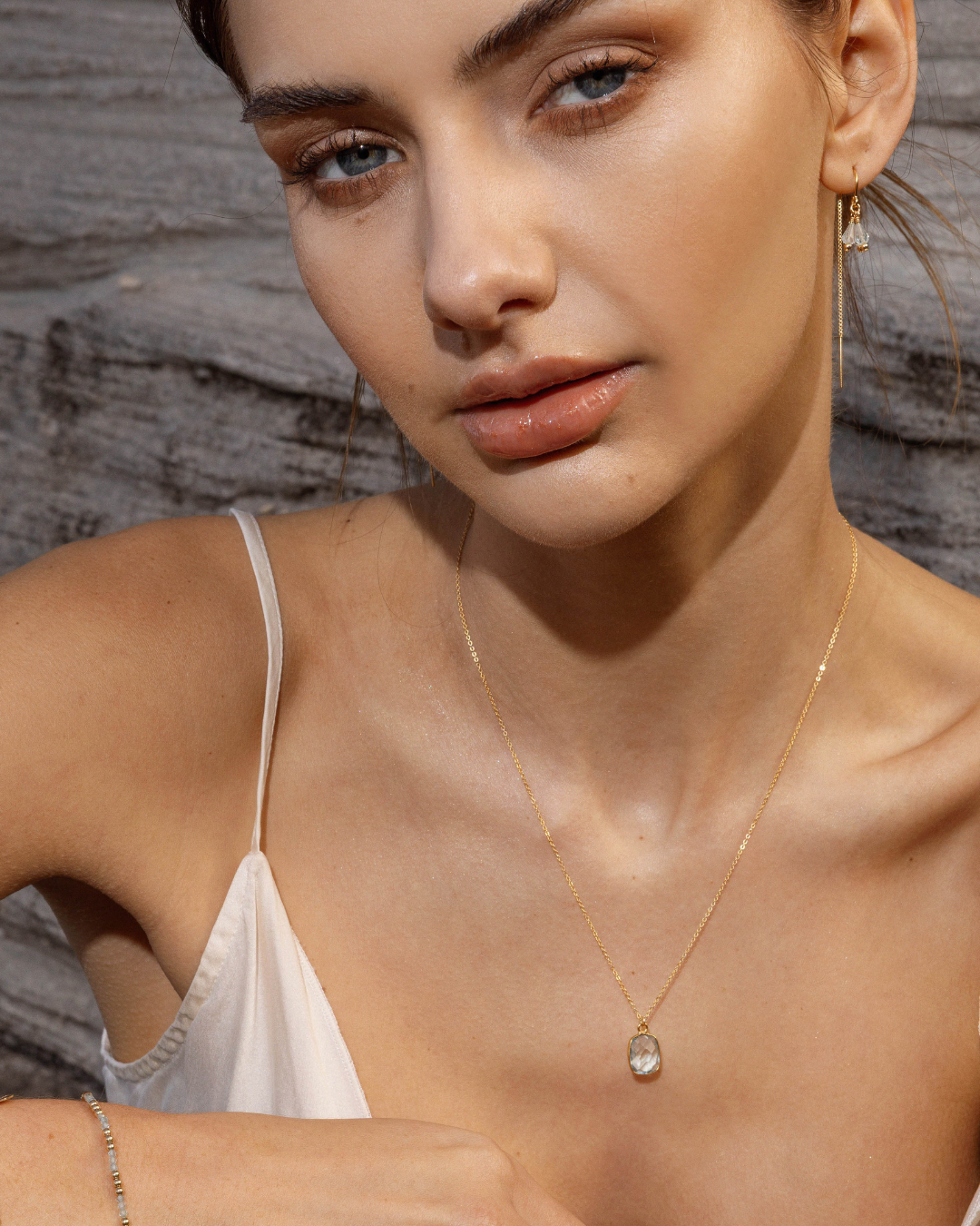 Close-up of a woman wearing a gold necklace with a pendant against a wooden background