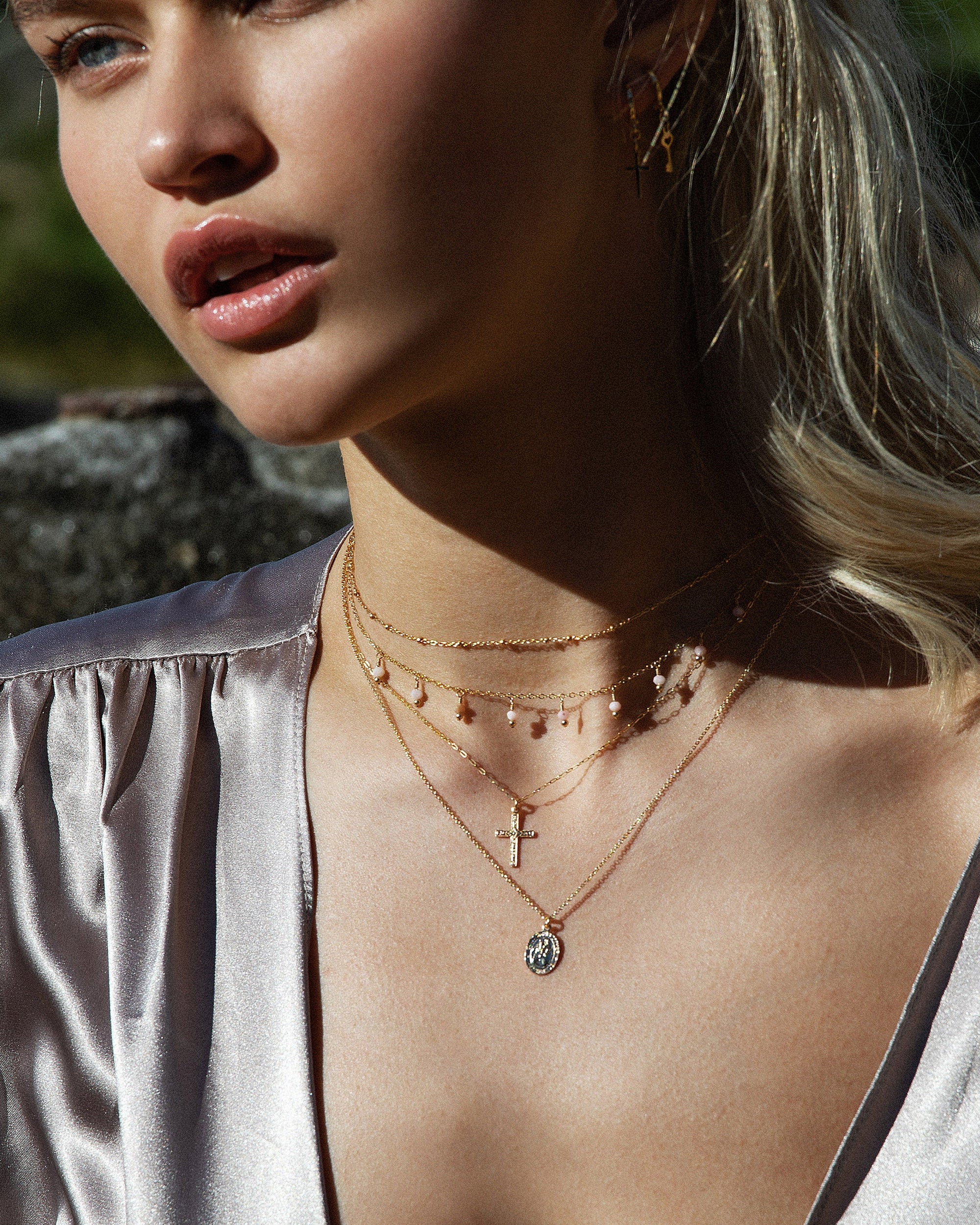 Woman wearing a silver blouse with layered necklaces including a cross pendant against a natural background