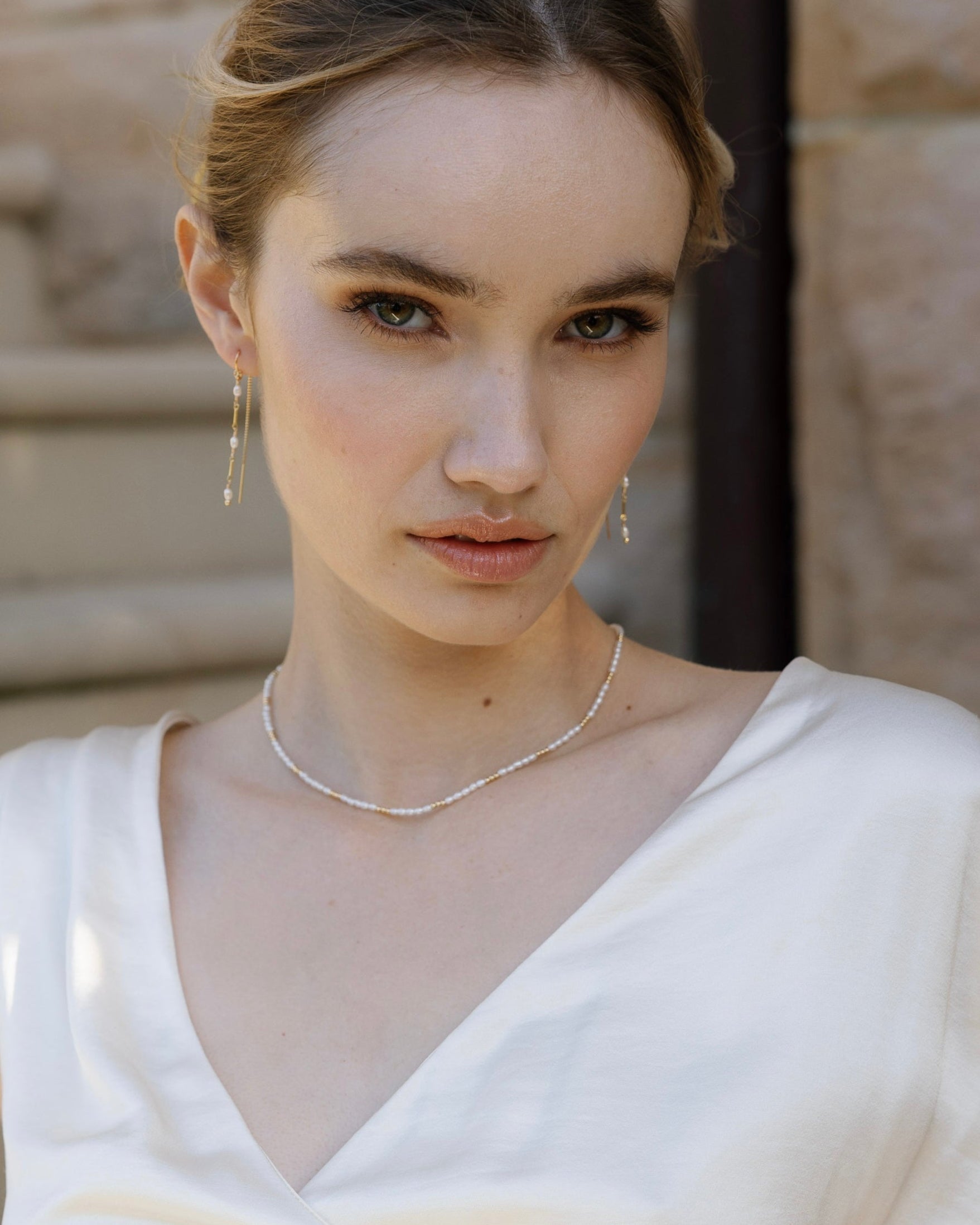 Bride in wedding dress wearing gold and pearl necklace and earrings with a neutral background