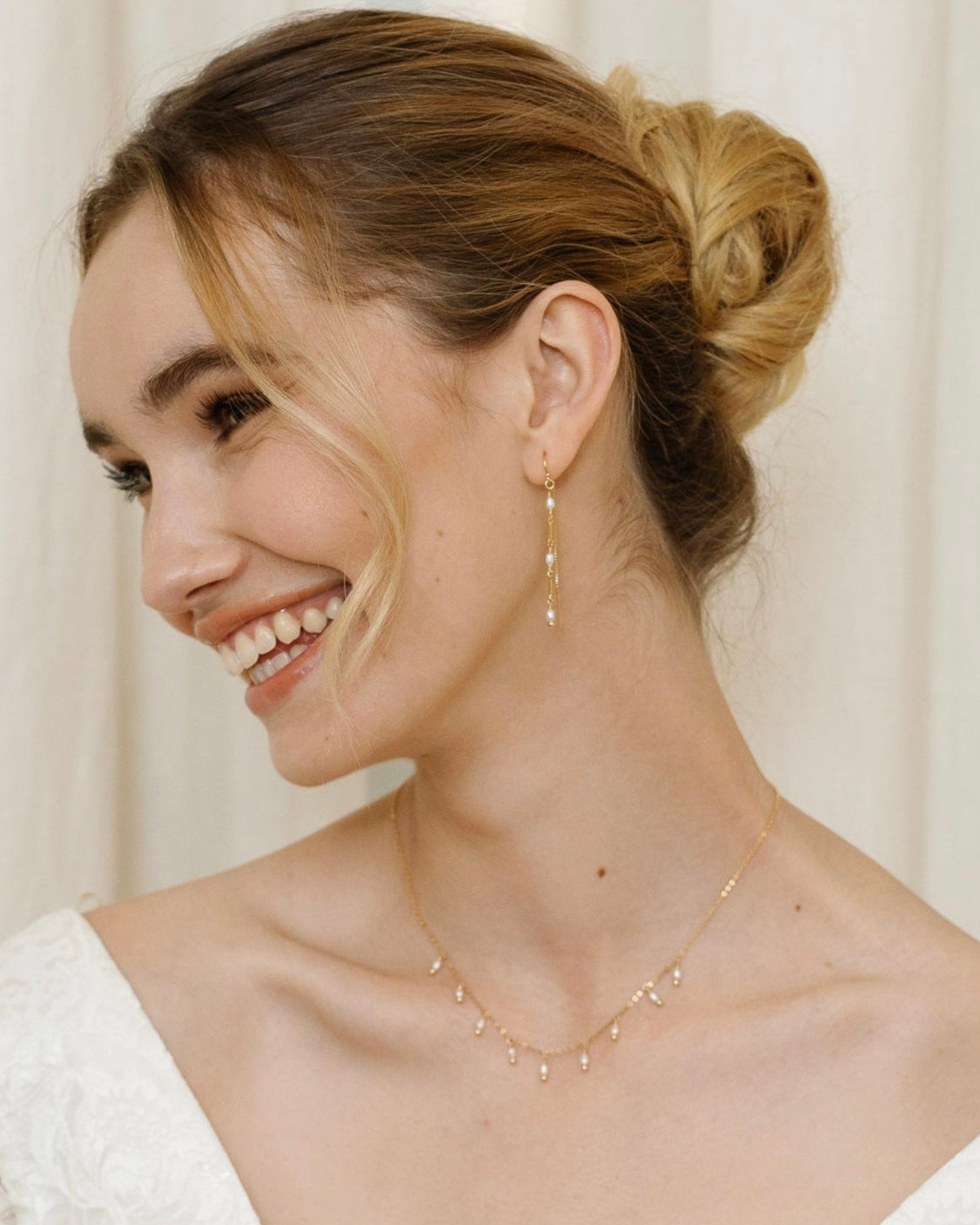 Bride wearing gold and pearl jewelry including earrings and a necklace against a neutral background