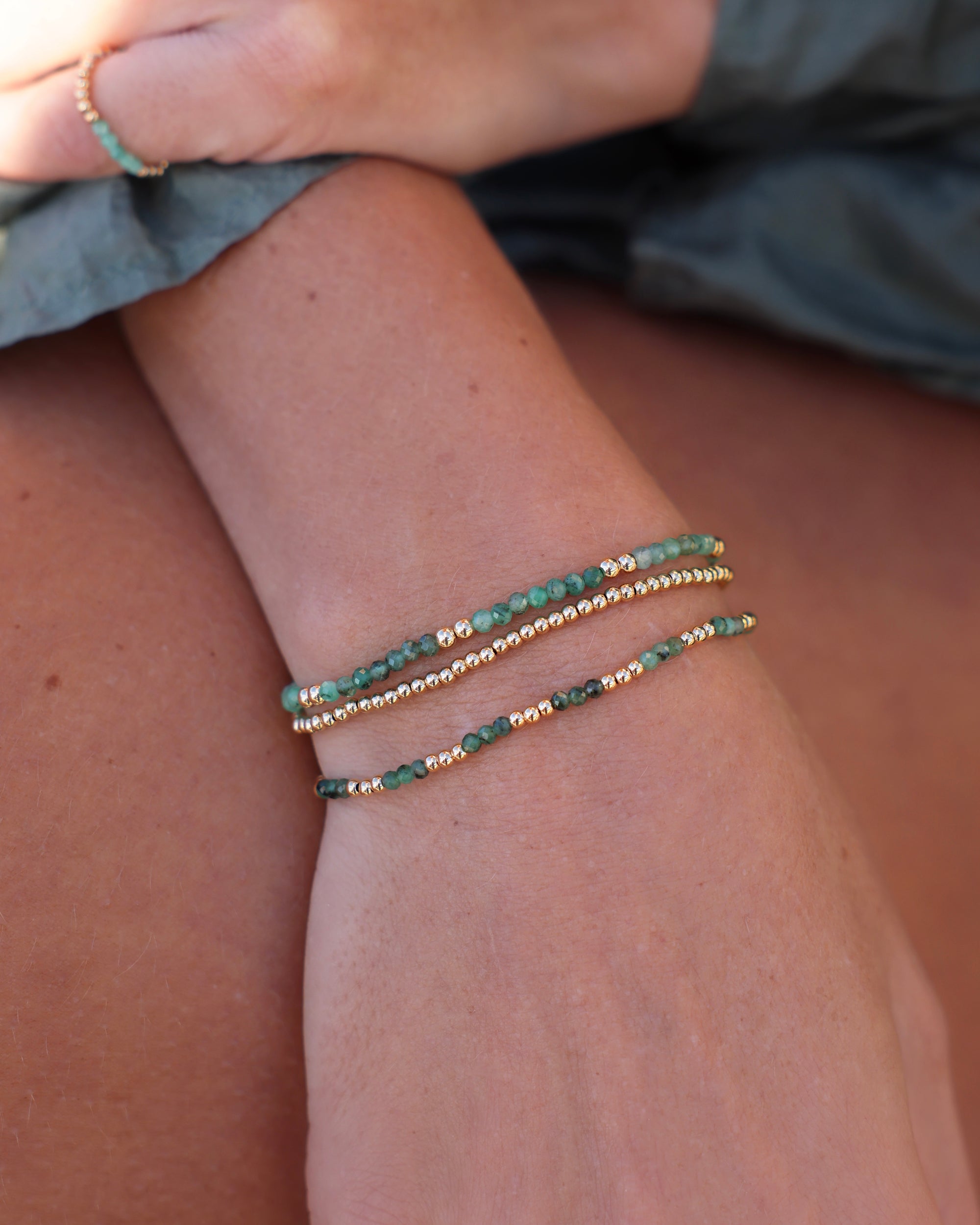 Close-up of a wrist wearing beaded bracelets with Emerald gemstones paired with smooth gold beads