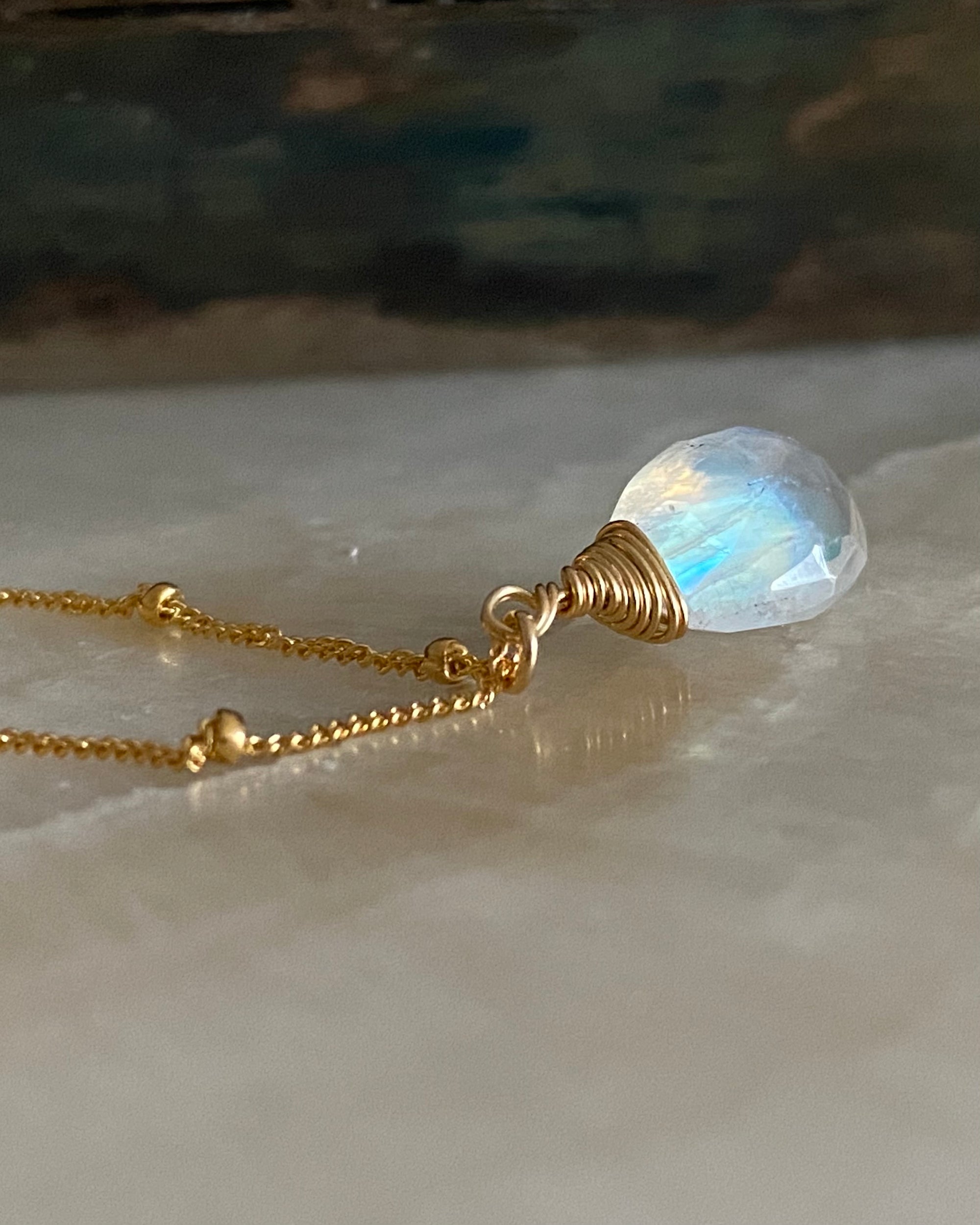 Necklace with a gold chain and moonstone pendant on a marble surface