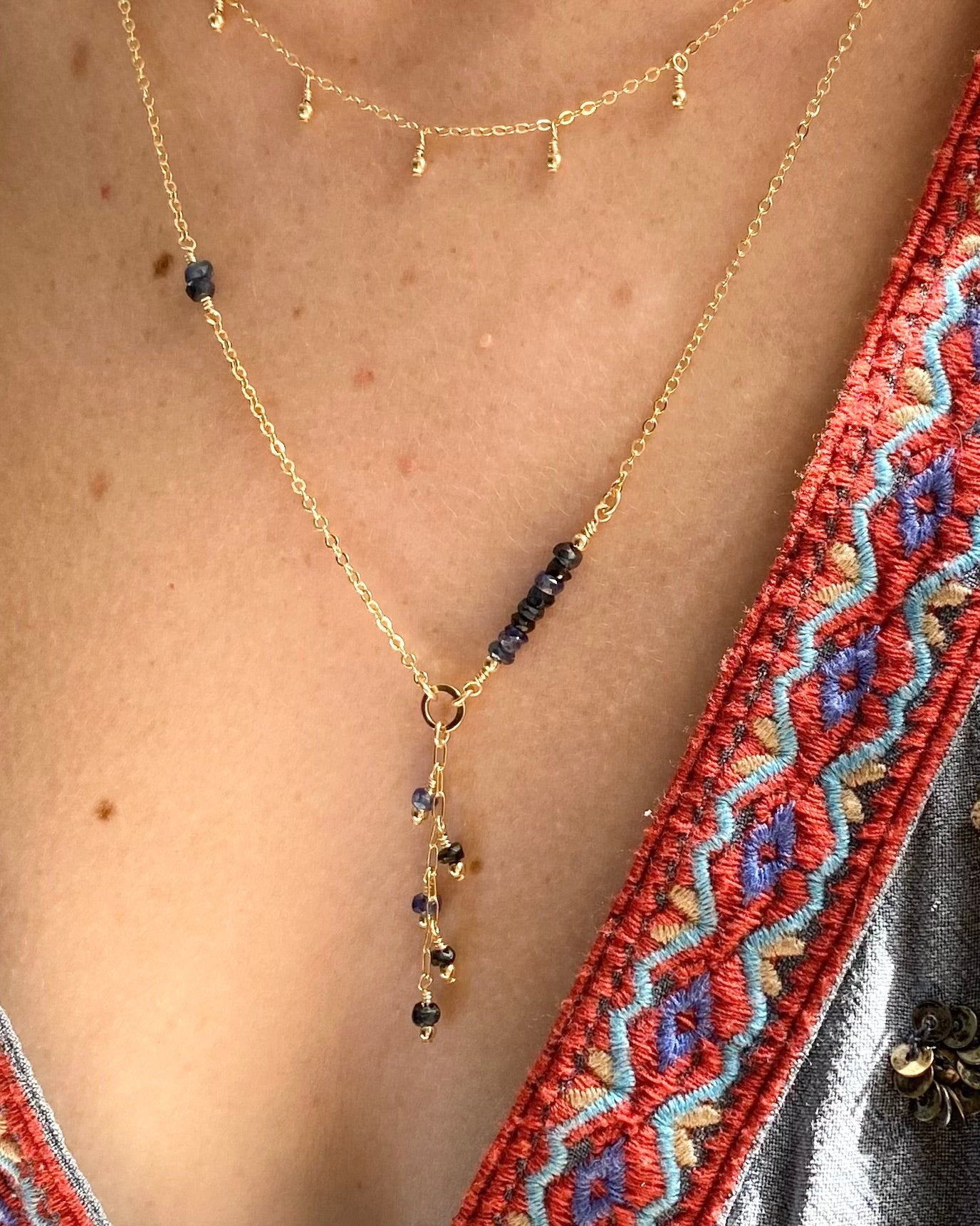 Gold necklace with sapphire beads on a person wearing a red and blue embroidered garment.