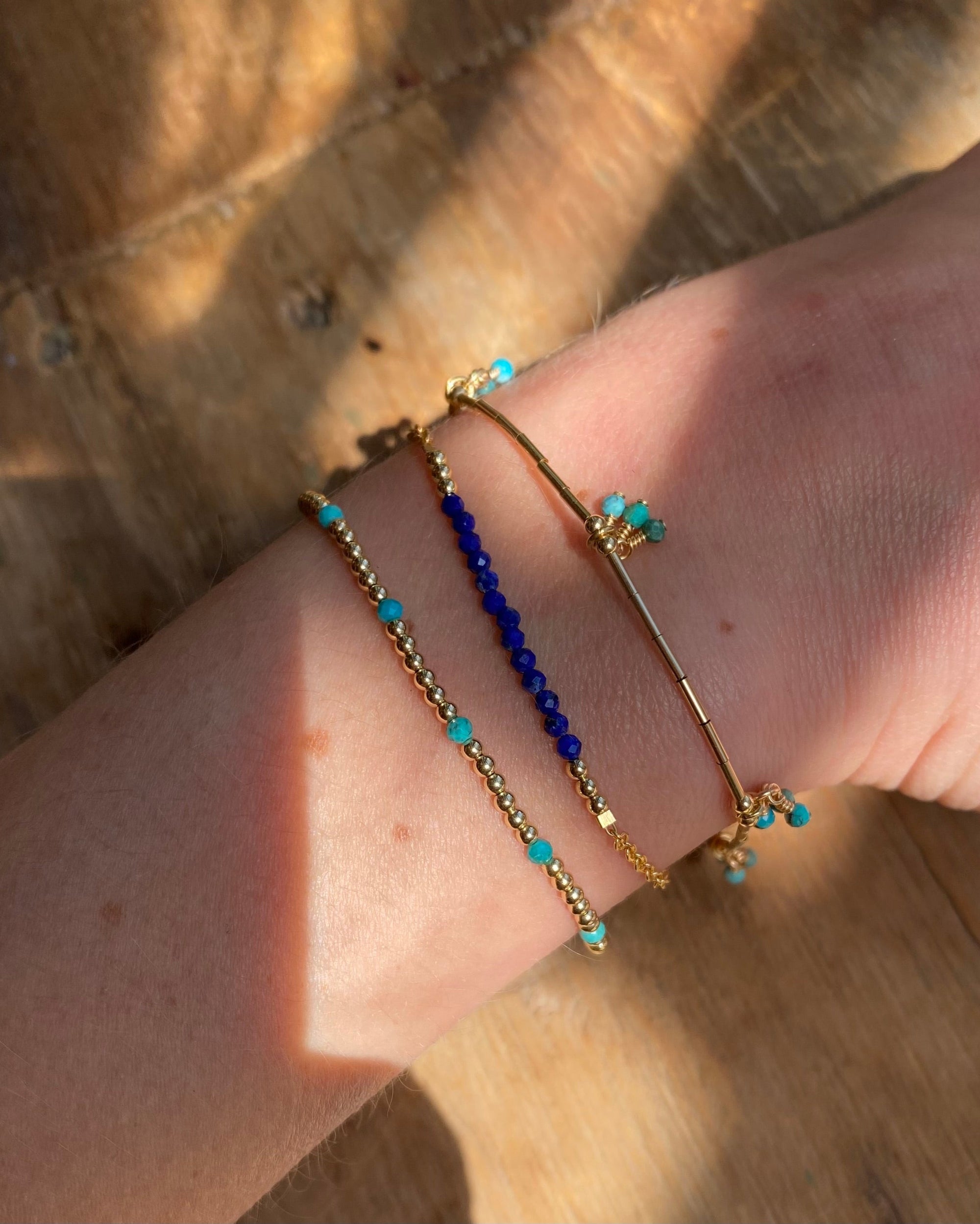 Close-up of a wrist wearing multiple bracelets with lapis lazuli and turquoise on a wooden surface