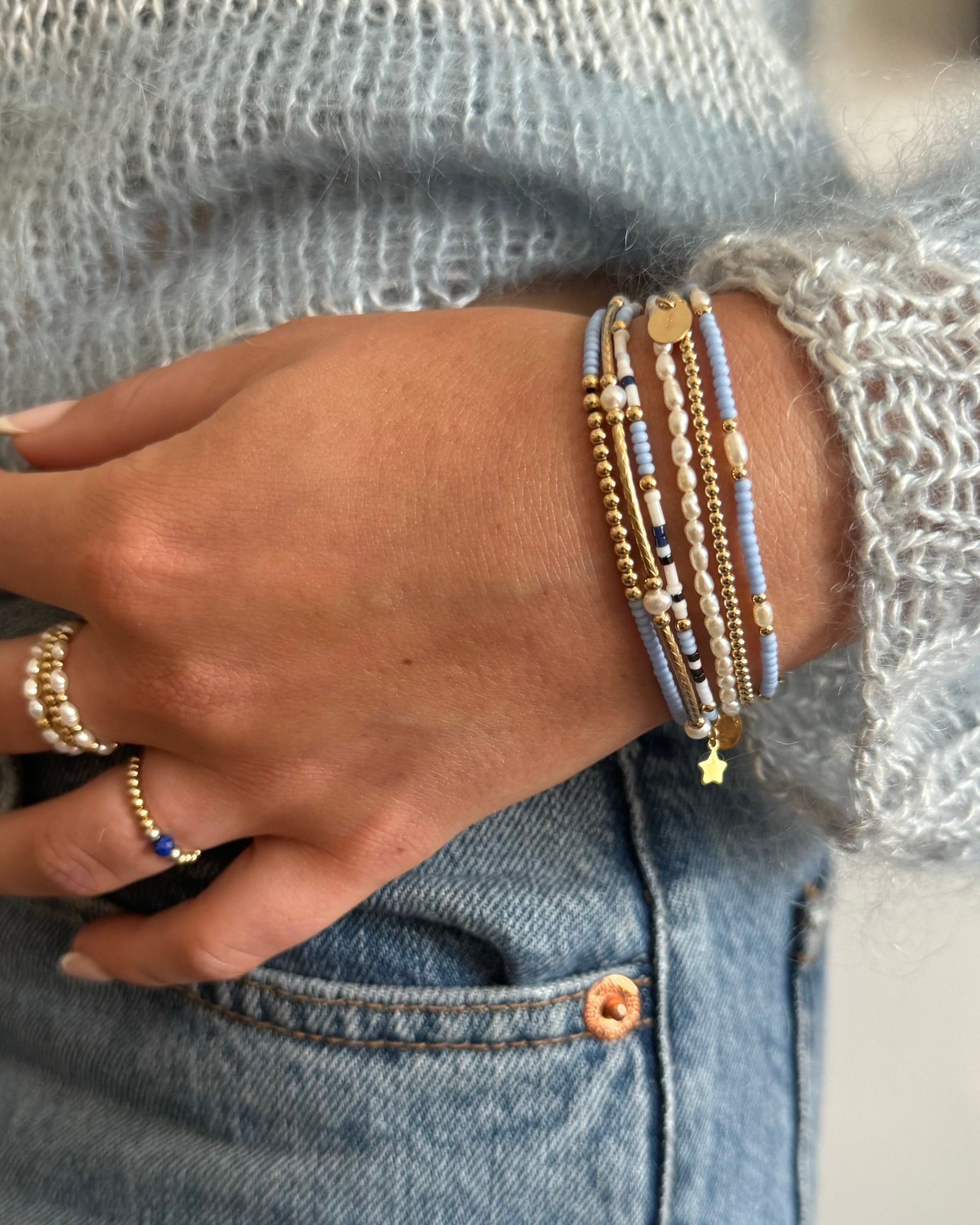 Models hand wearing multiple gold beaded bracelets with glass beads and pearls.  Also wears pearl rings.