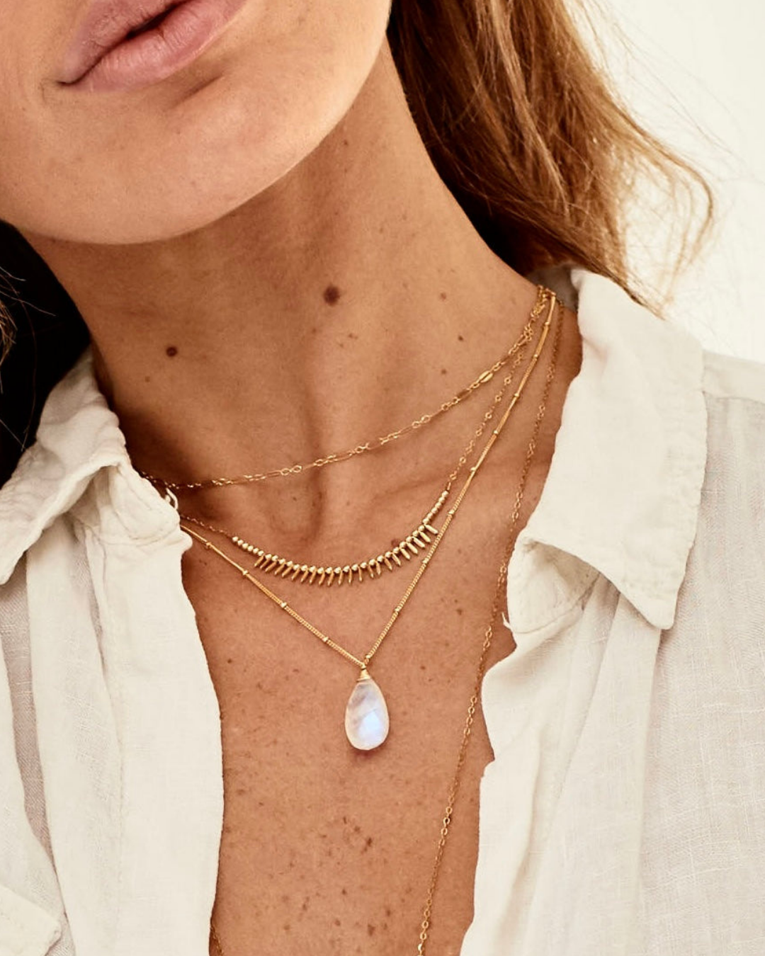 Close-up of a female model wearing layered gold necklaces with a white shirt.