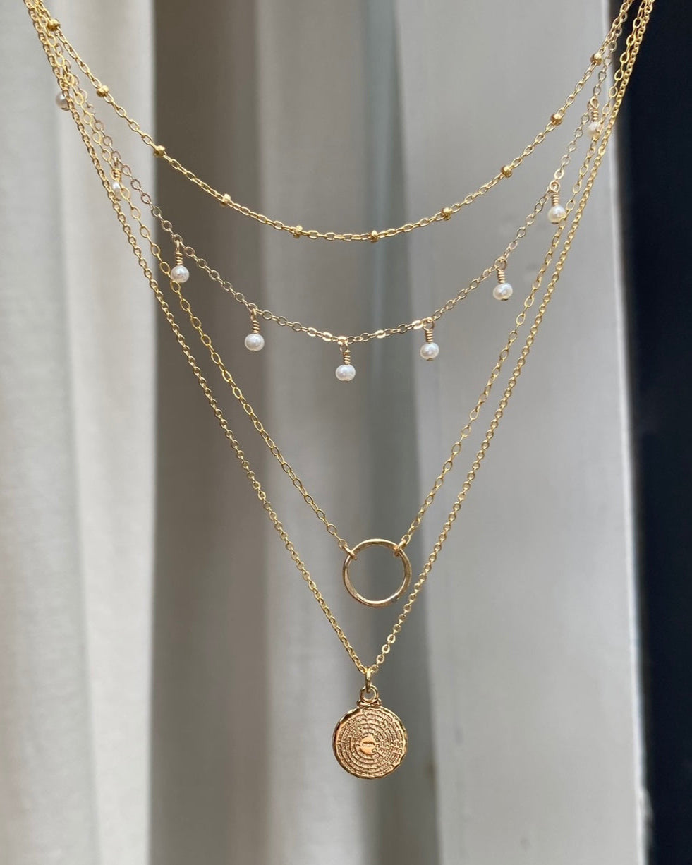 Three gold necklaces with pearl pendants on a neutral background