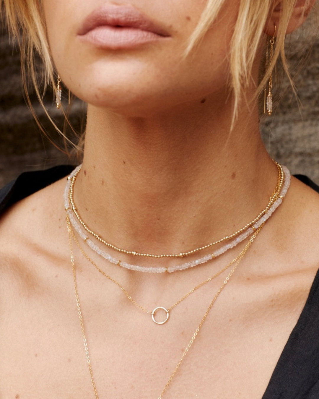 Close-up of a female wearing layered  multiple gold necklaces with a blurred background
