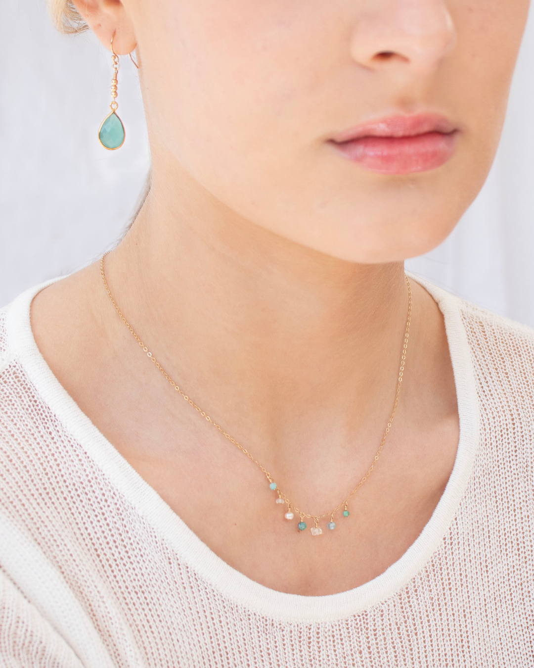 Close-up of a person wearing a delicate necklace with small aqua gemstones and a pair of Chalcedony earrings.