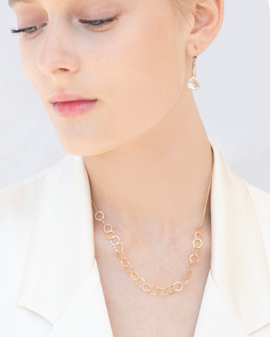 Gold earrings with green amethyst earrings and a gold chain necklace worn by a person on a plain background
