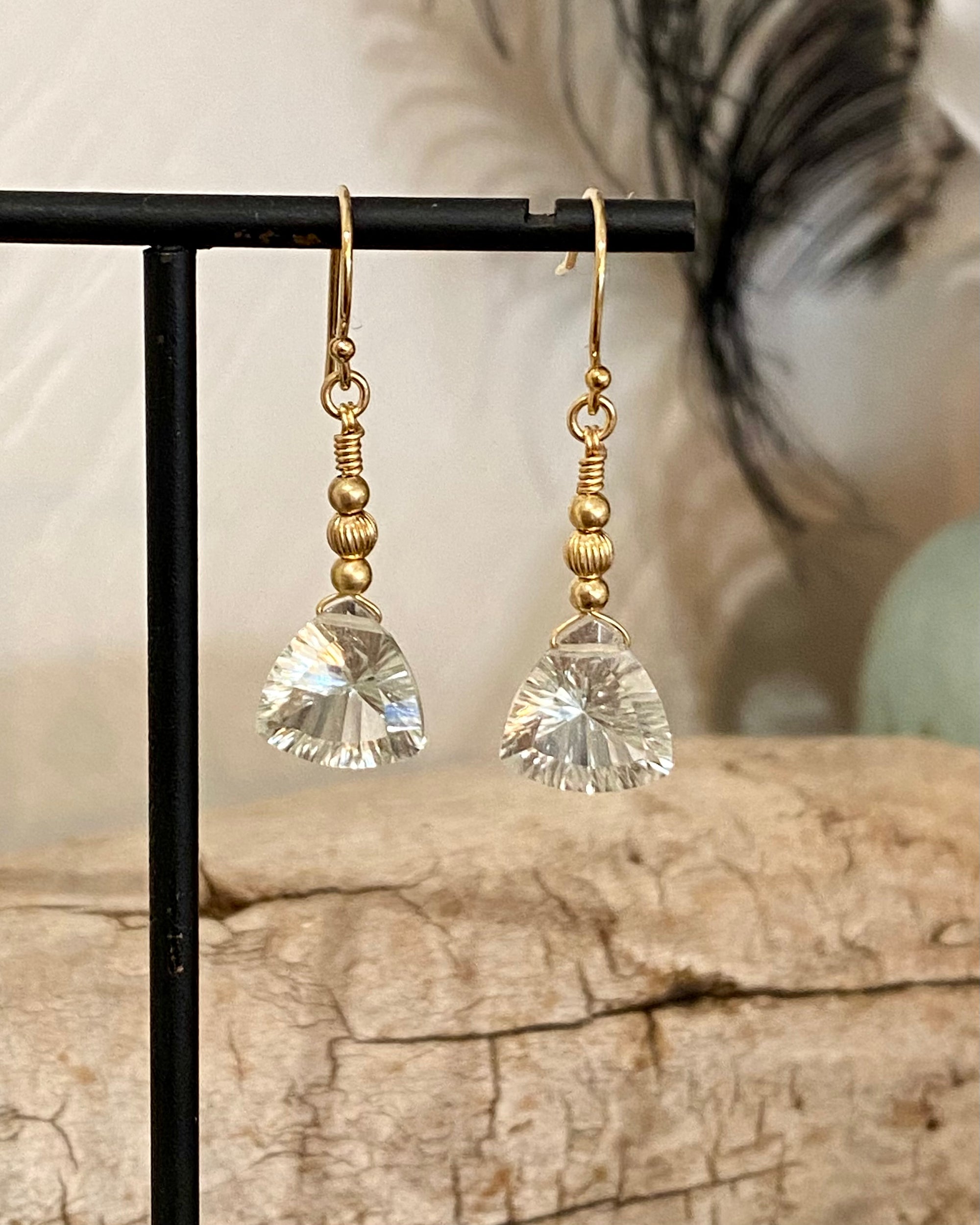 Pair of gold and green amethyst drop earrings on a black stand with a natural background.