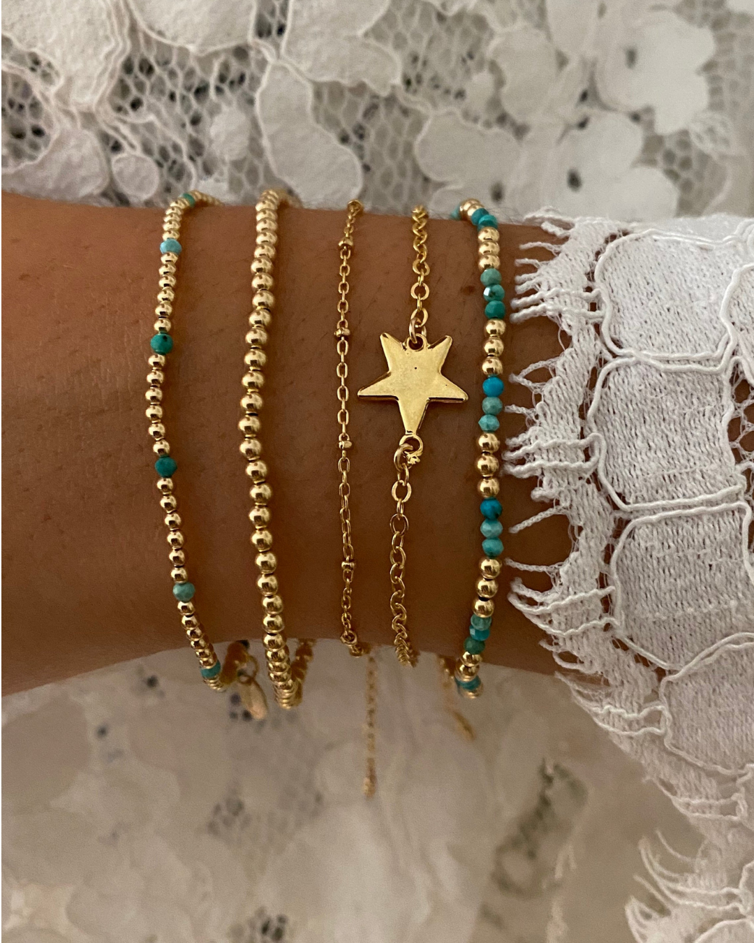 Gold layered bracelets on a close up of wrist against lace clothing