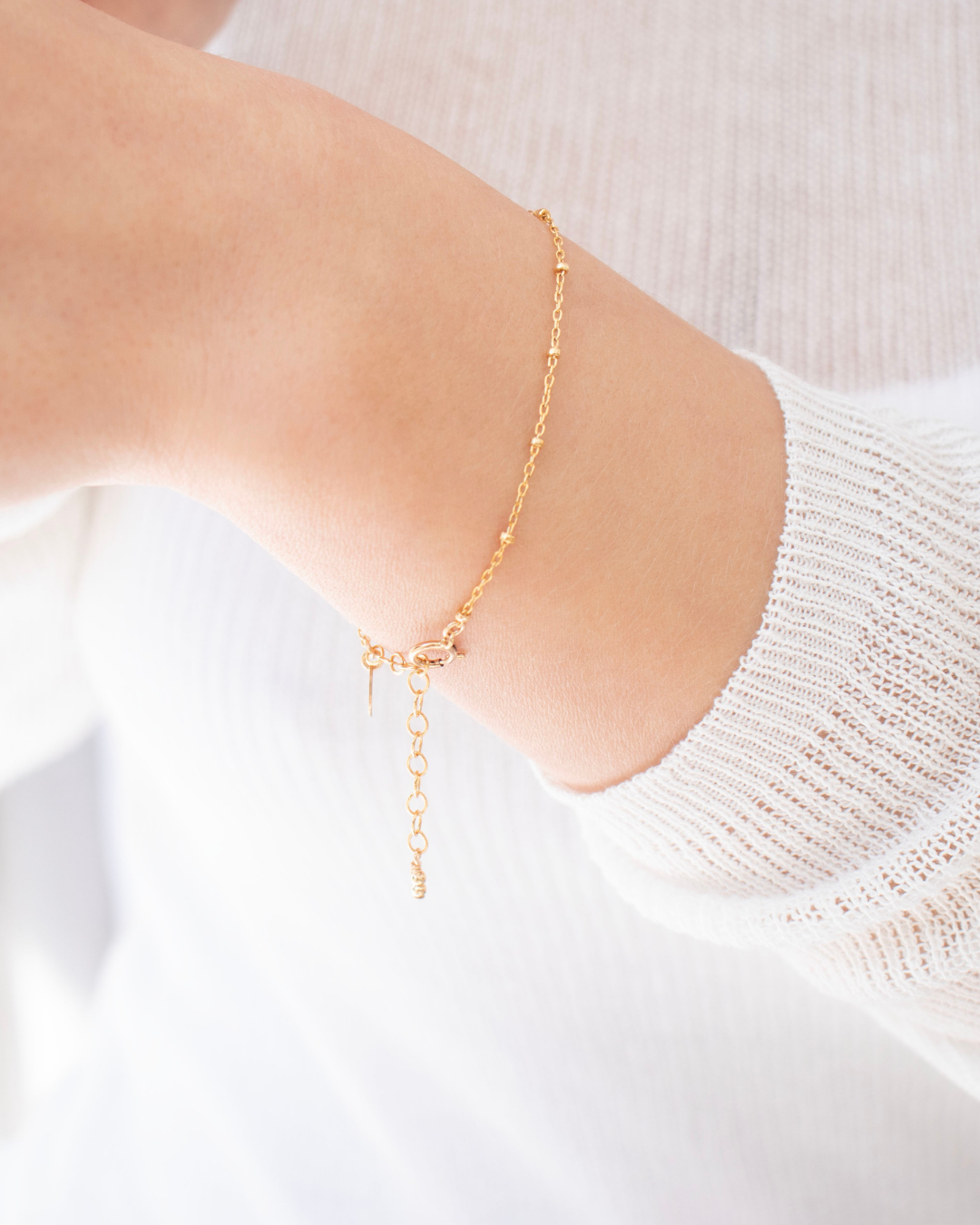 Gold fine gold ball chain bracelet on a models wrist with a light background