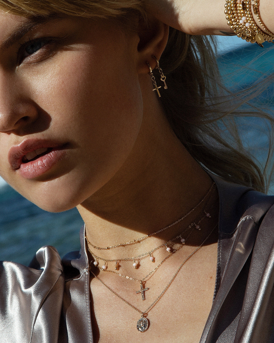 Close-up of a woman wearing gold layered necklaces bracelets and earrings with a blurred background