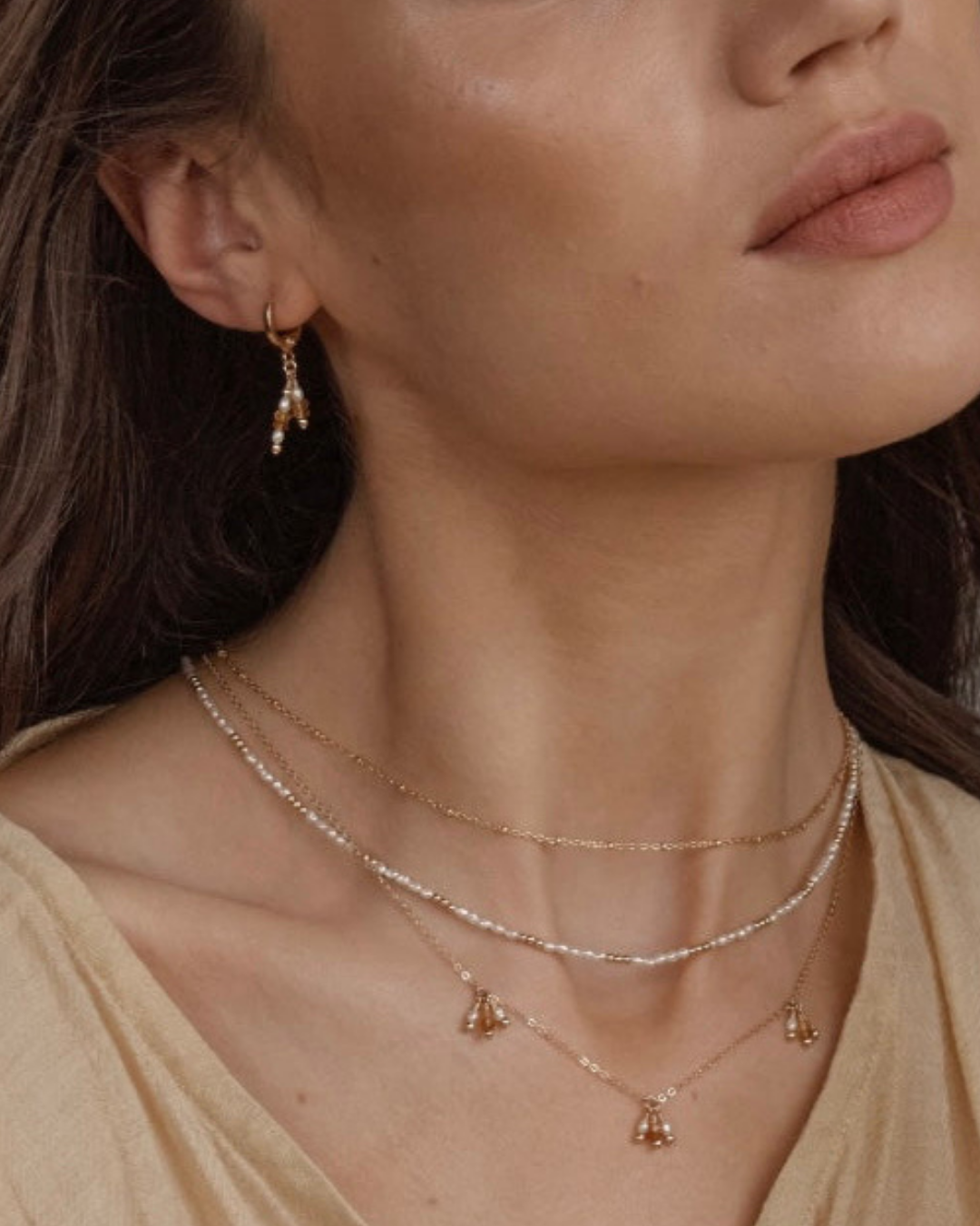 Close-up of a woman wearing gold necklaces and earrings with pearl and citrine gemstones.

