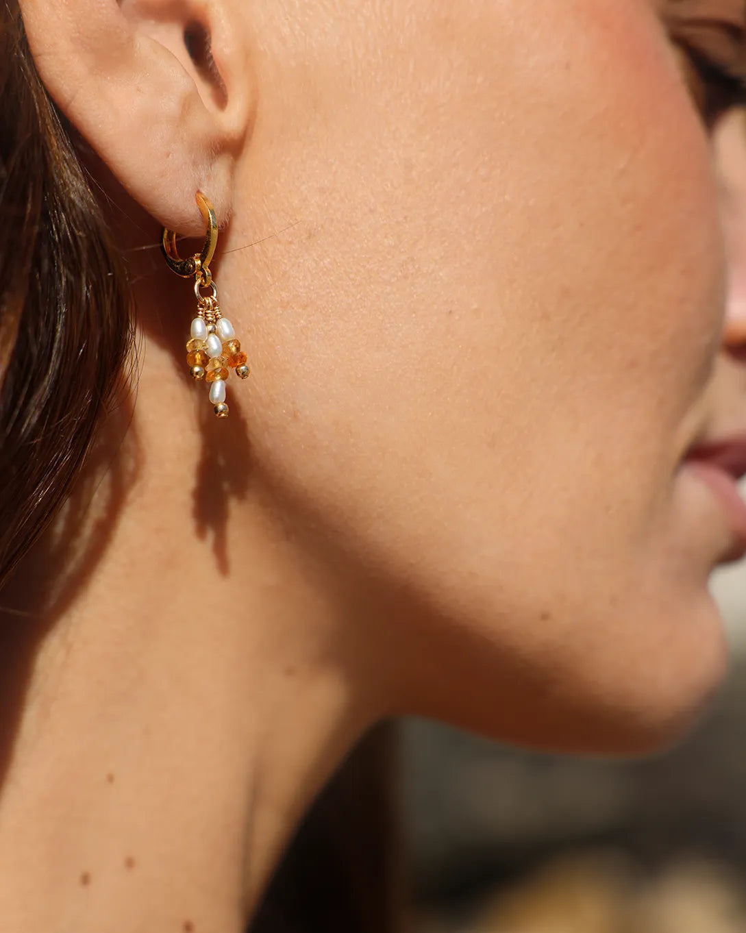 Close-up of a model wearing gold earrings with Citrine gems and freshwater seed Pearls.