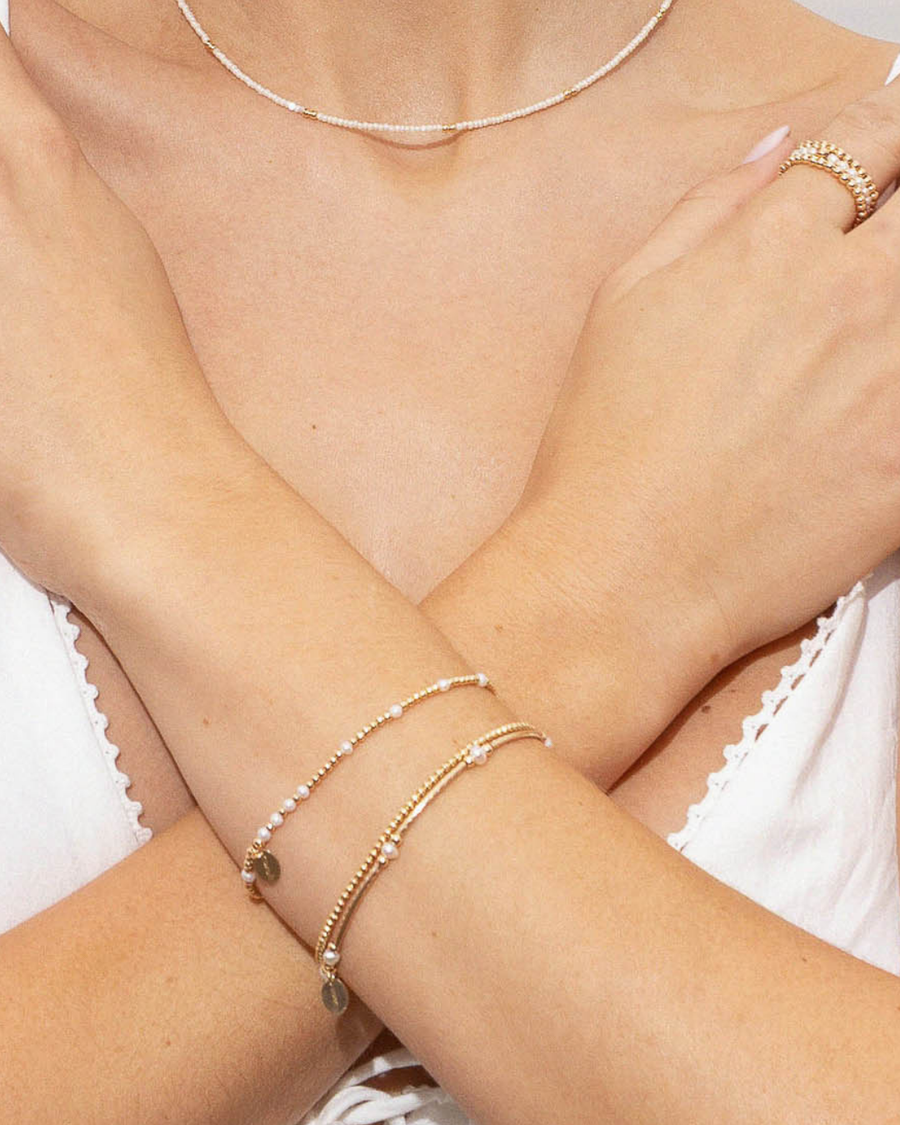 Close-up of a person's arms wearing gold and pearl bracelets necklace and earrings.