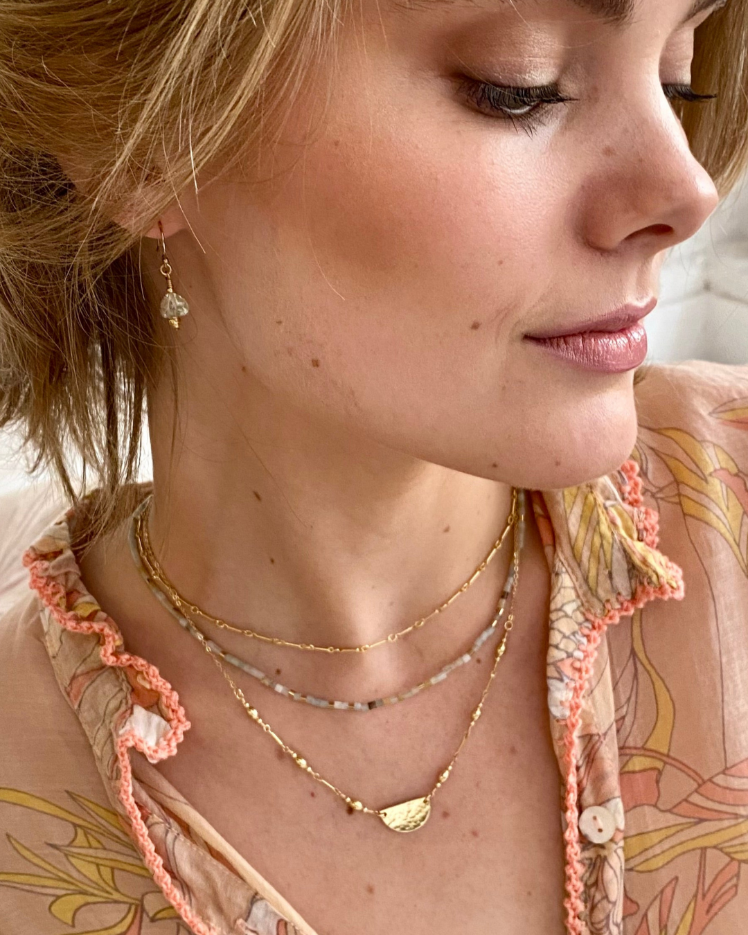 Close-up of a woman wearing multiple gold necklaces and an earring.
