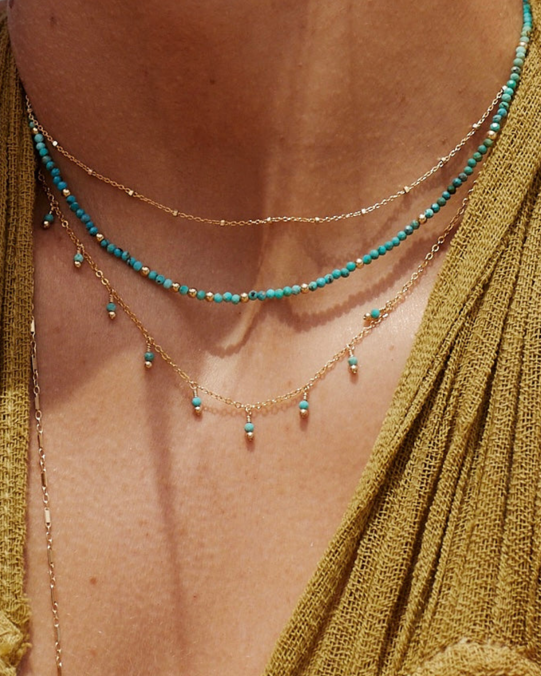 Close-up of a person's neck wearing a turquoise beaded necklace with layered gold chains.