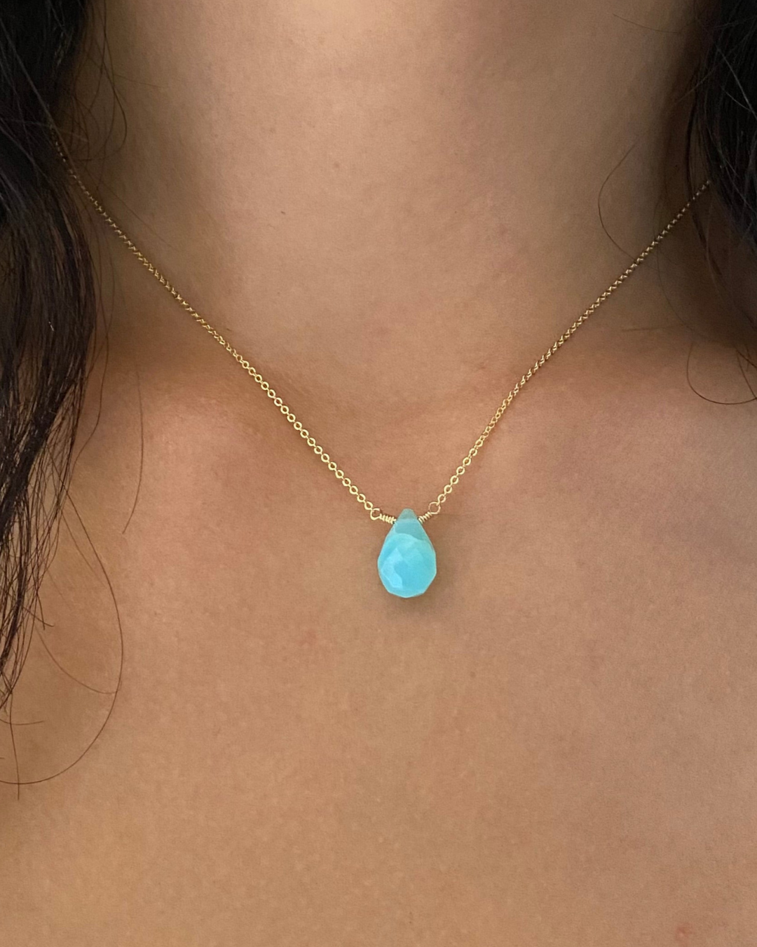 Close up of woman's neck with a blue Peruvian opal teardrop pendant on a gold chain necklace.