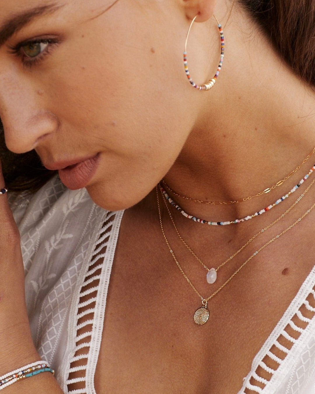 Close-up of a woman wearing gold necklaces including Moonstone pendant and hoop earrings.