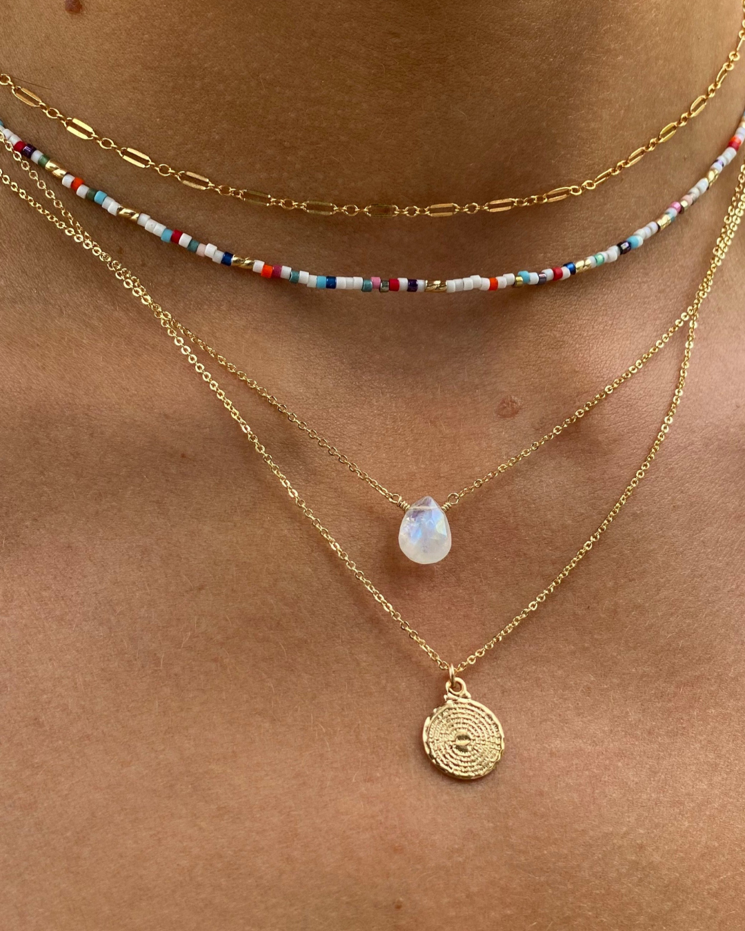 Close-up of a woman's neck wearing multiple gold necklaces including Moonstone pendant.