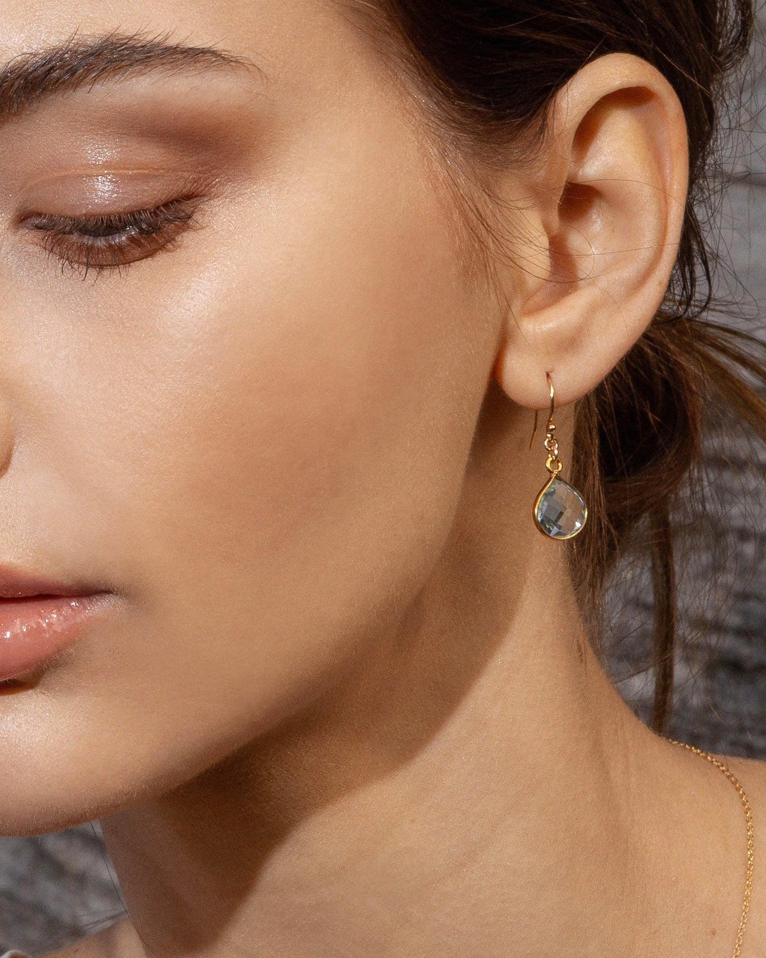 Close-up of a woman wearing gold earrings with aquamarine gemstone.