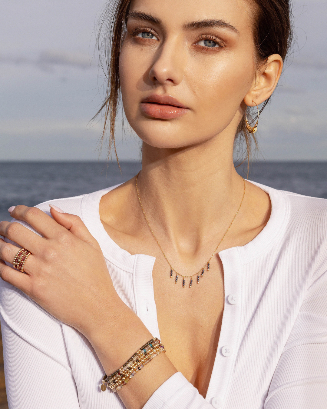 Woman wearing gold jewellery including a necklace with black spinel beads with a ocean background