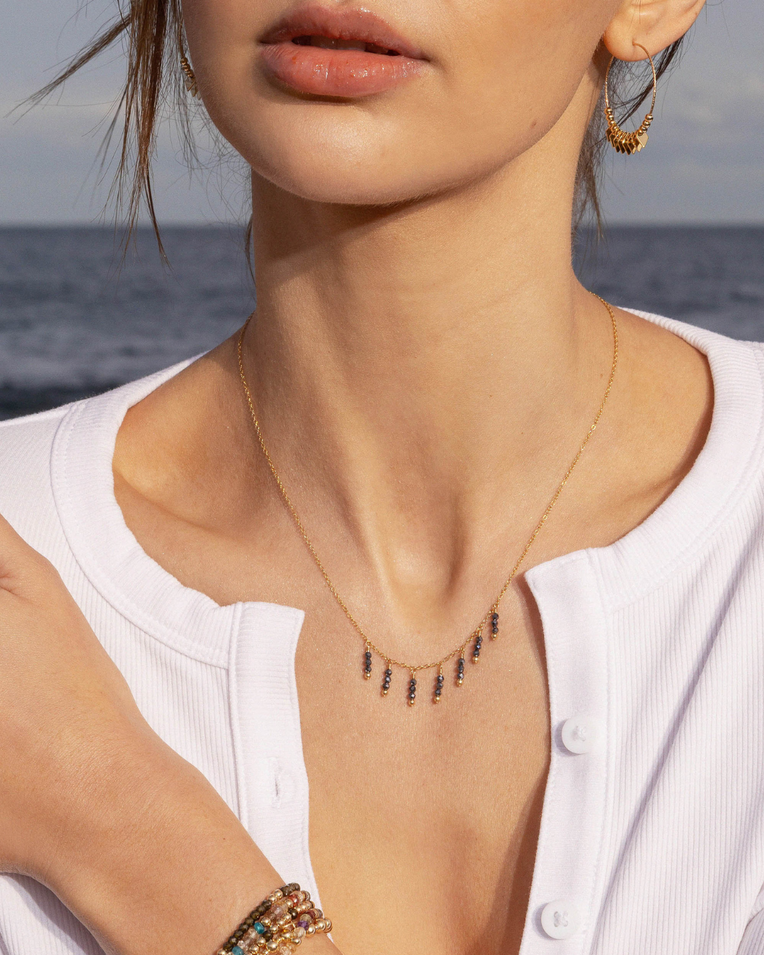 Close-up of a woman wearing a delicate necklace with black spinel beads with ocean background